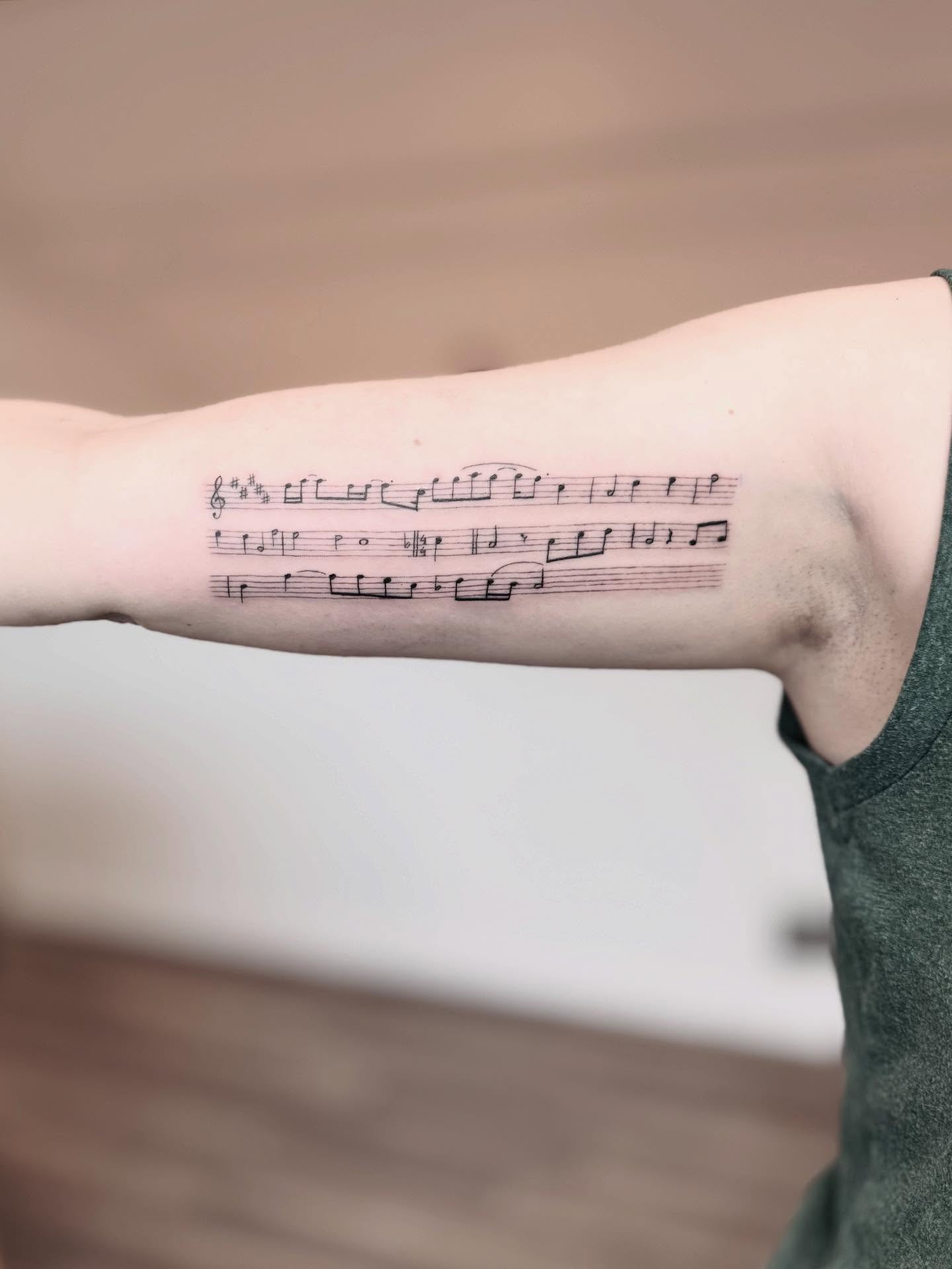 Sheet music black and grey tattoo on the forearm by Jessica Abbey