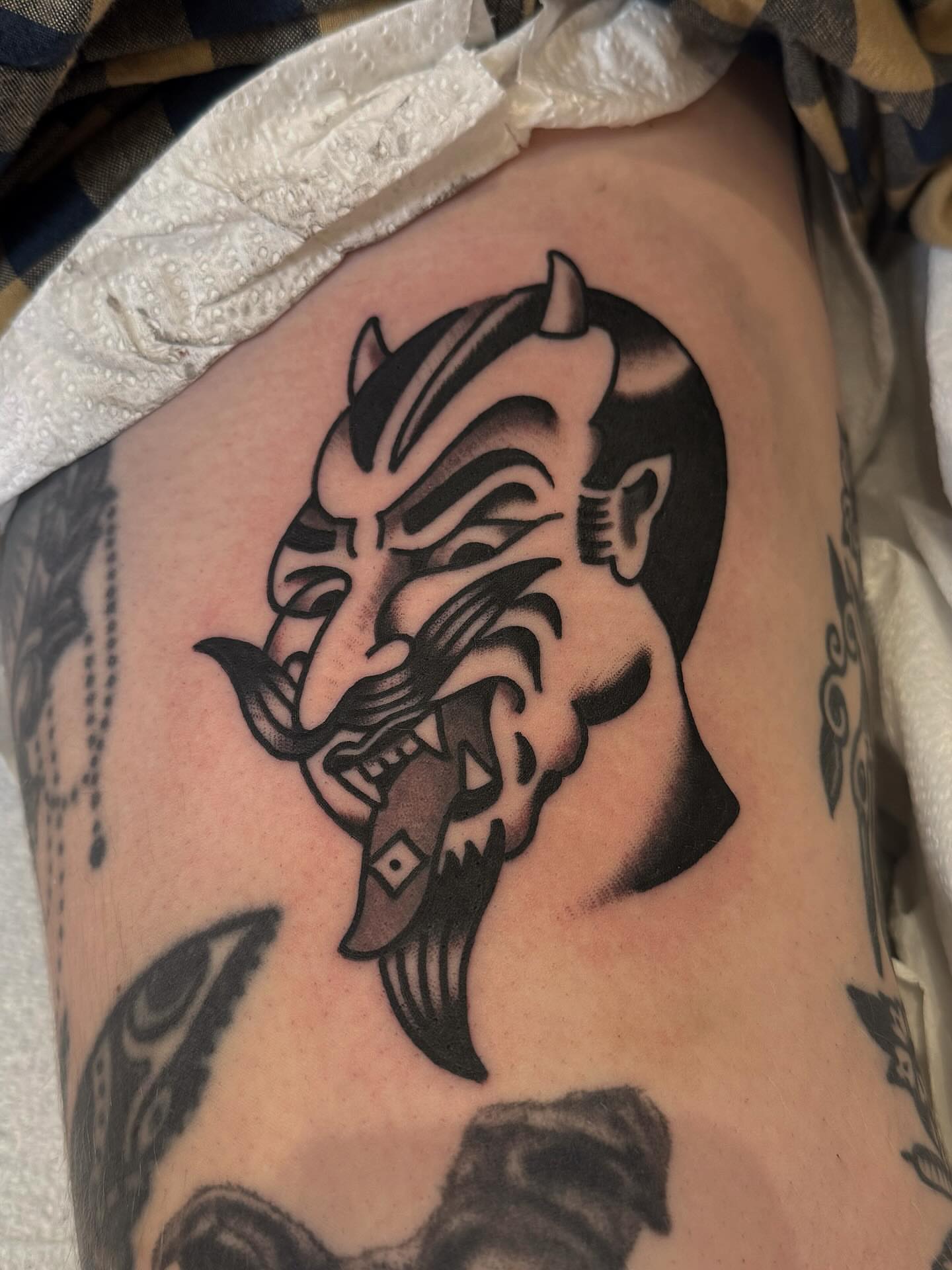 Demon mask black and grey tattoo on the thigh by Bryce Shearer