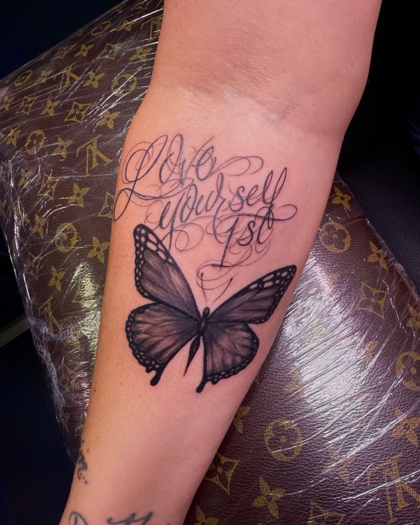 Love yourself 1st black and grey tattoo on the forearm by Germaine Sherman