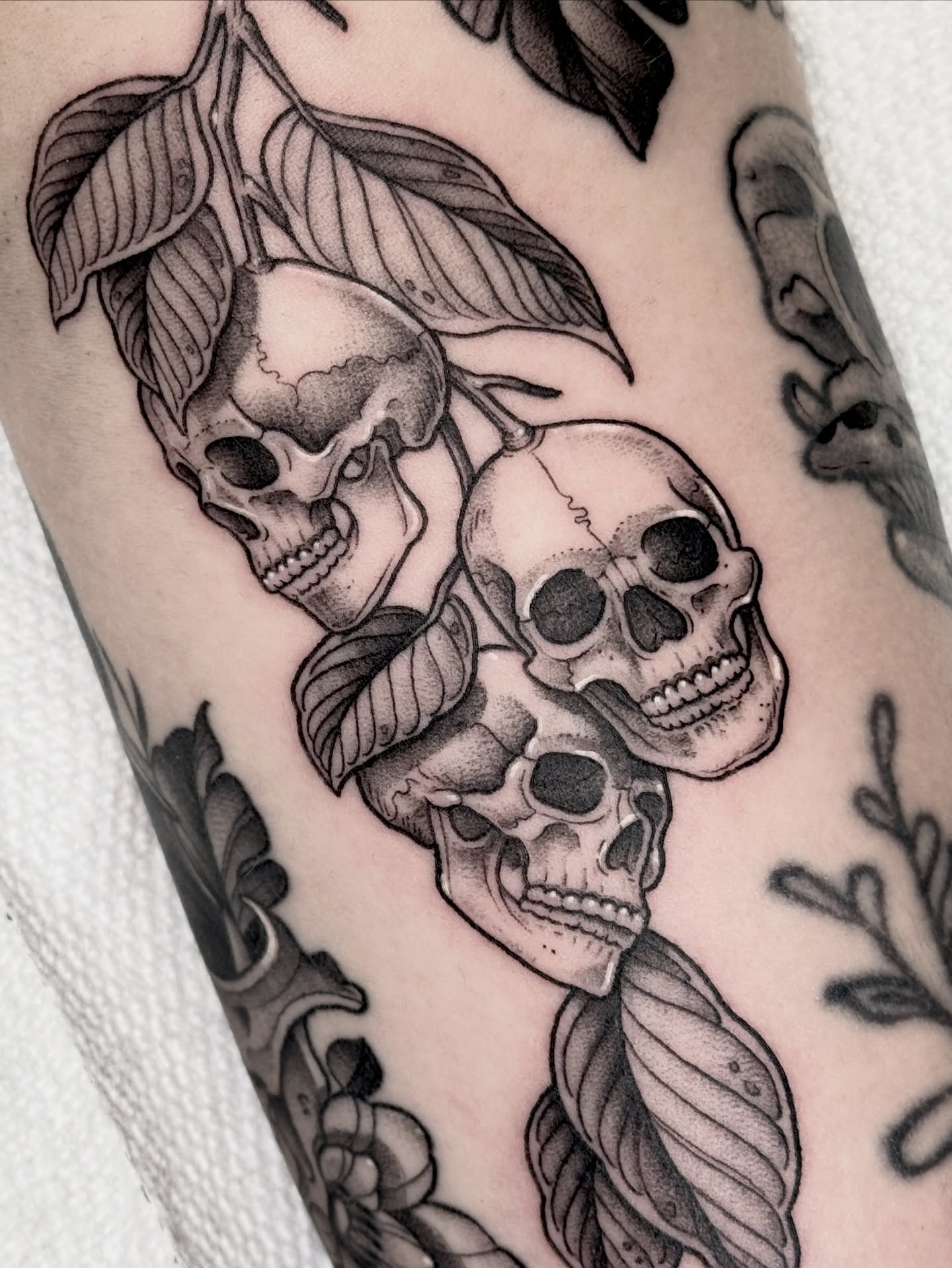 Skulls and leaves black and grey tattoo on the forearm by Hannah May, La Mesa, California