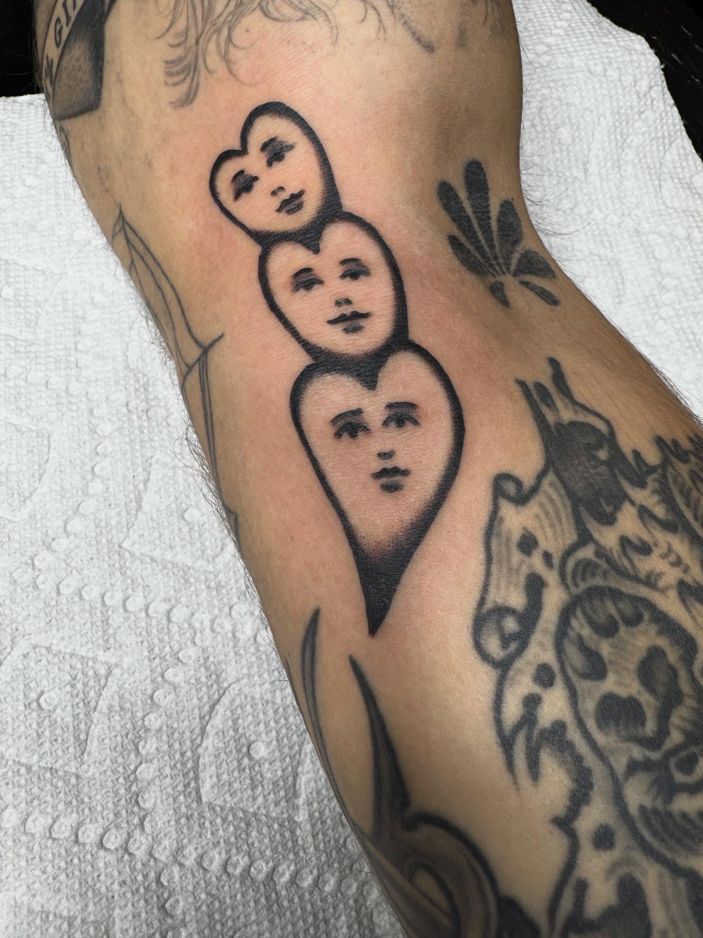 Hearts with faces black and grey tattoo on the forearm by JoJo Benton