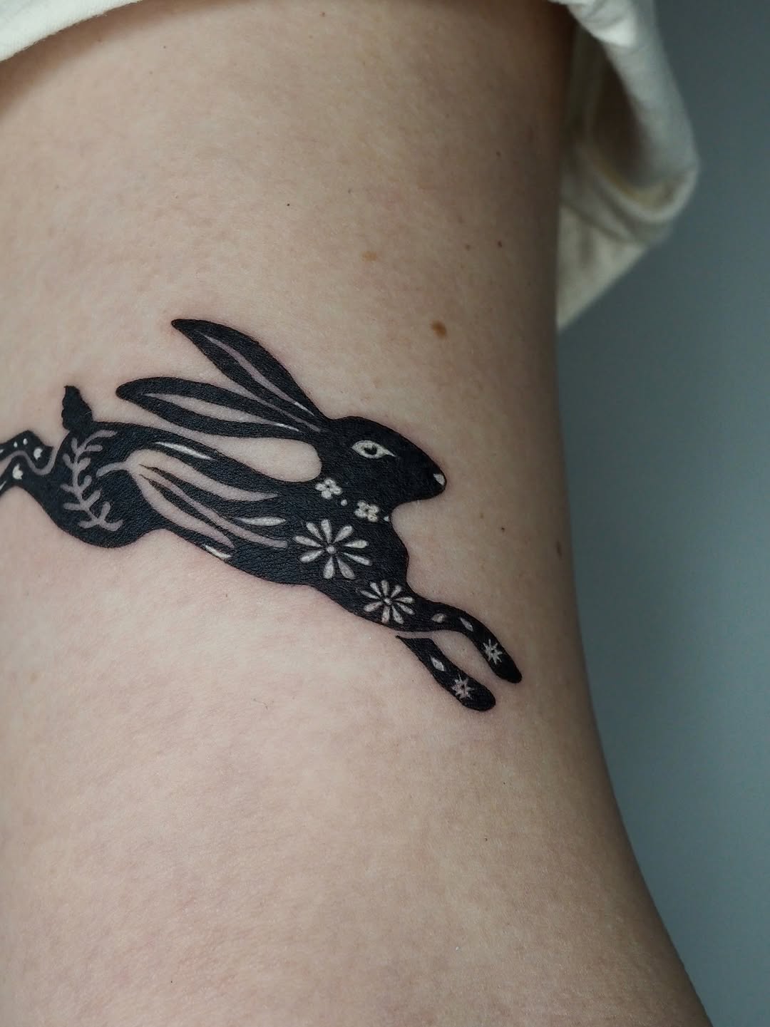 Running rabbit with floral pattern fine line tattoo on the forearm by A. Eye Tat