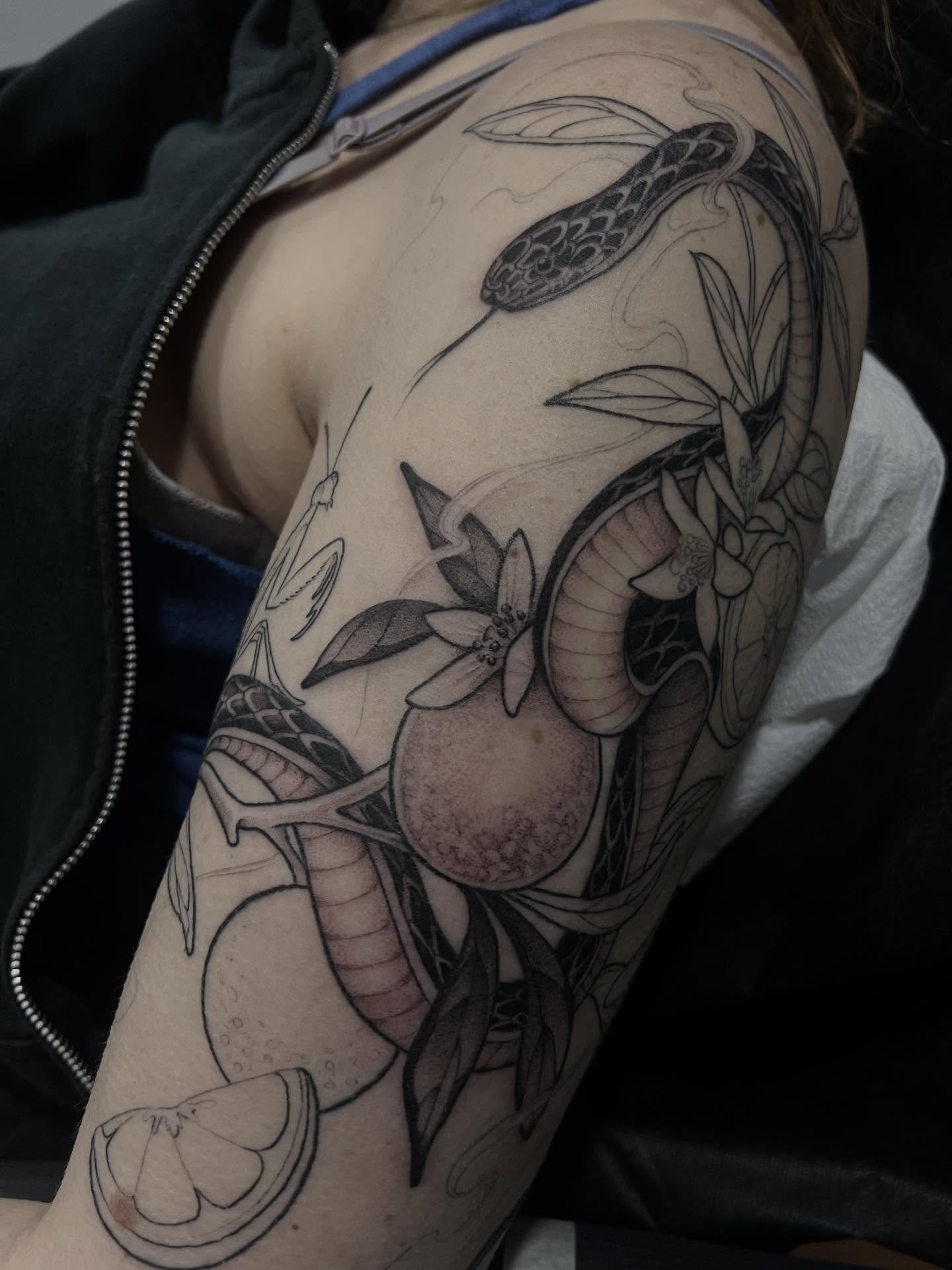 Snake and fruit black and grey tattoo on the upper arm by Avrey Simone