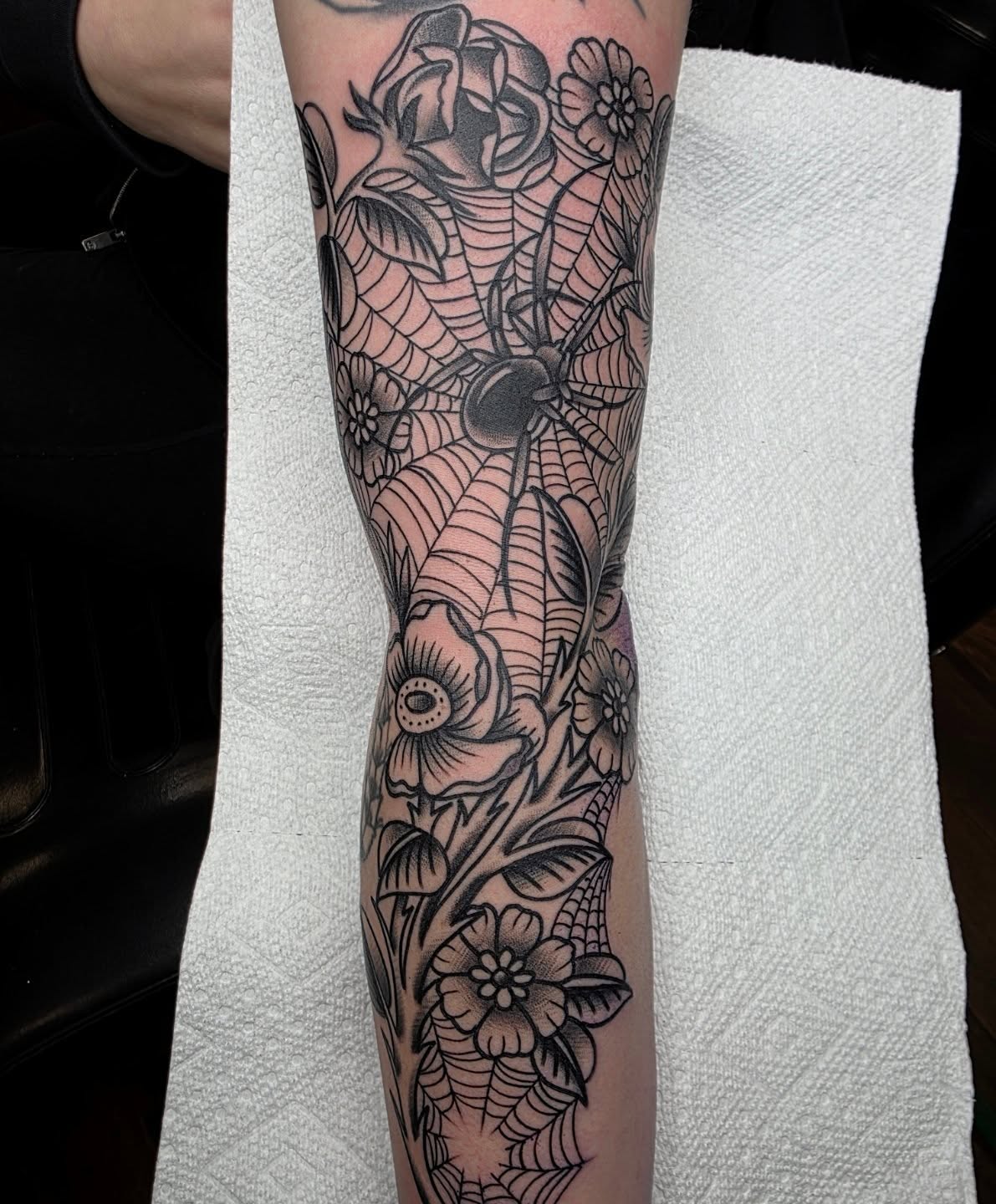 Spider and floral bouquet black and grey tattoo on the forearm by Adam Garnek