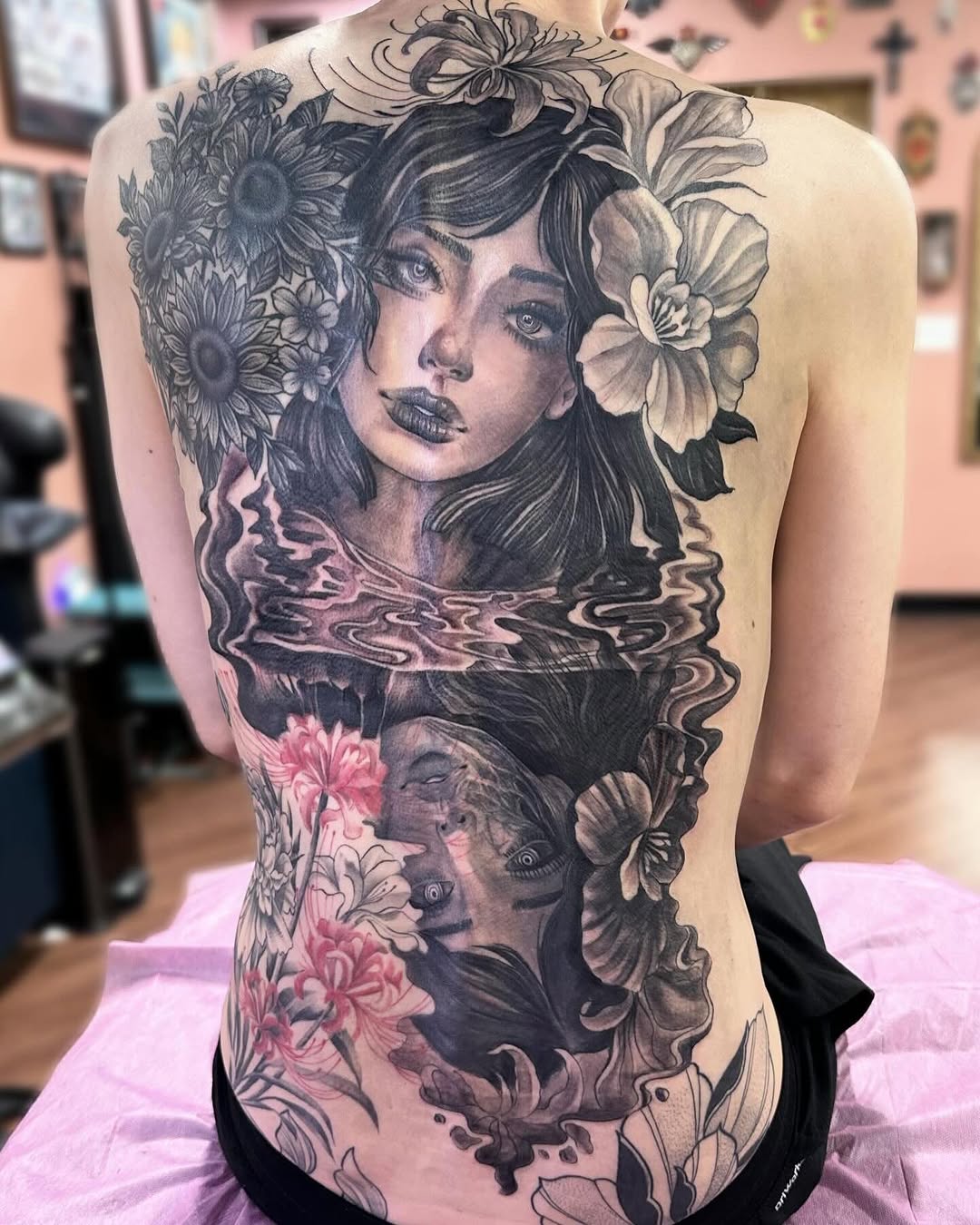 Woman with flowers and submerged face realism tattoo on the back by Mathilda Quynh