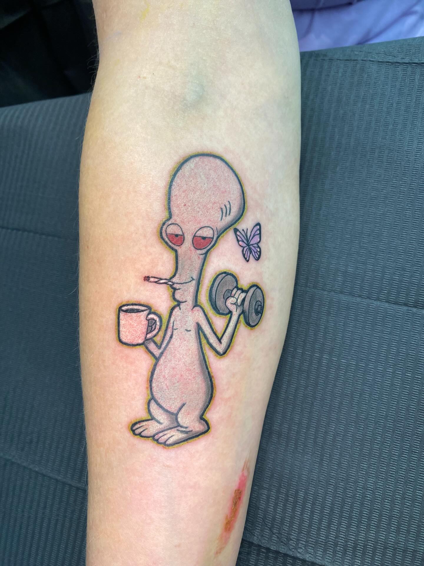 Alien lifting weights illustrative tattoo on the forearm by @dom_macio_tattoo