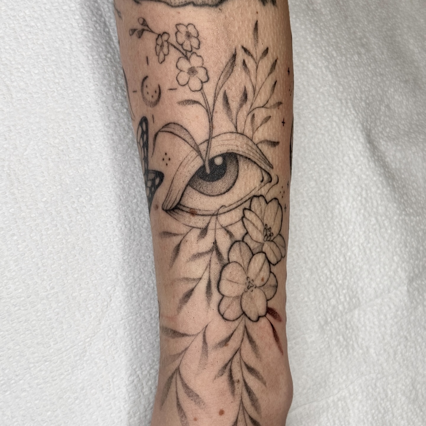 Eye and floral arrangement black and grey tattoo on the forearm by Molly Murray