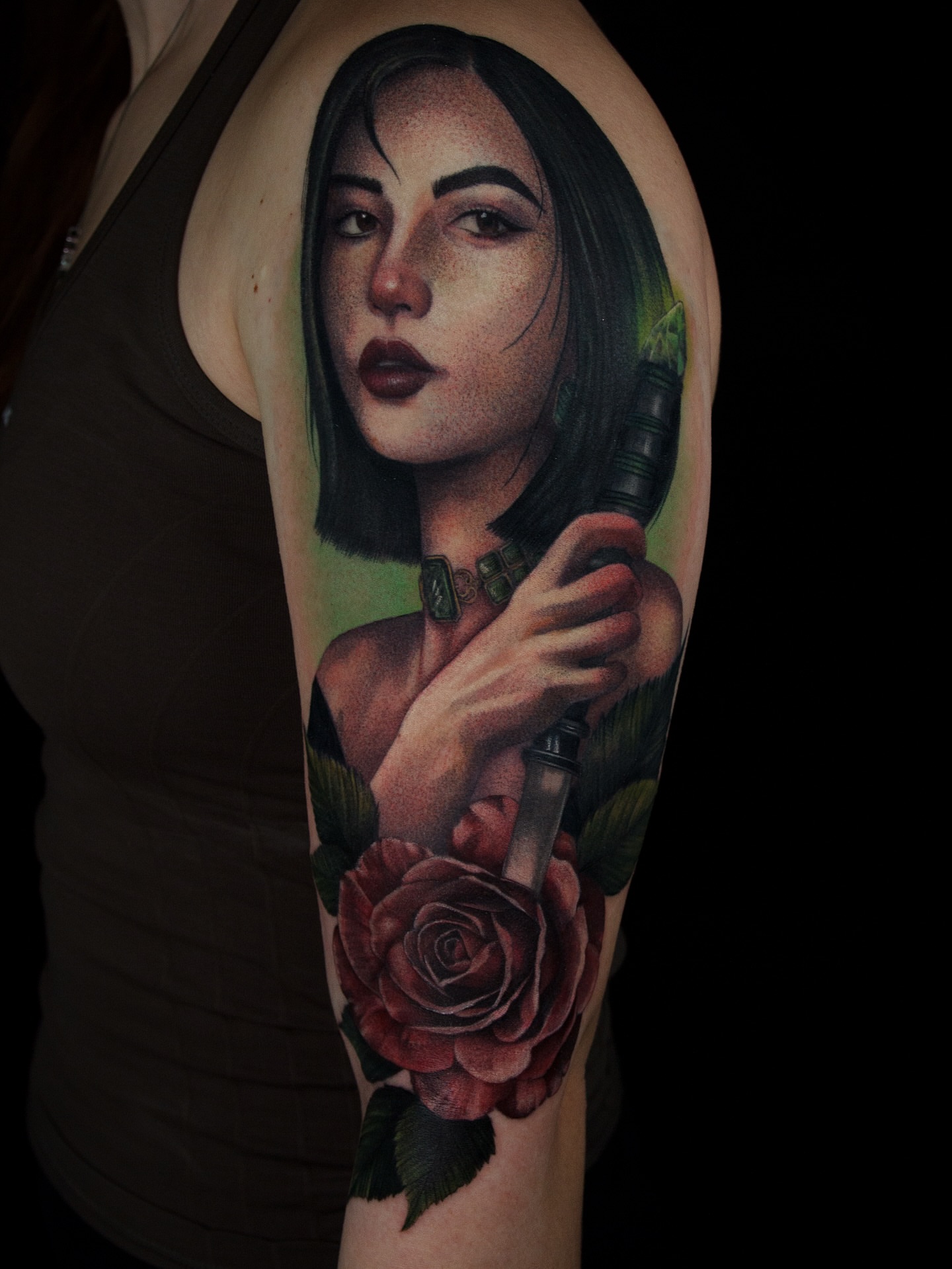 Woman with gun and rose realism tattoo on the upper arm by caliope yiannos