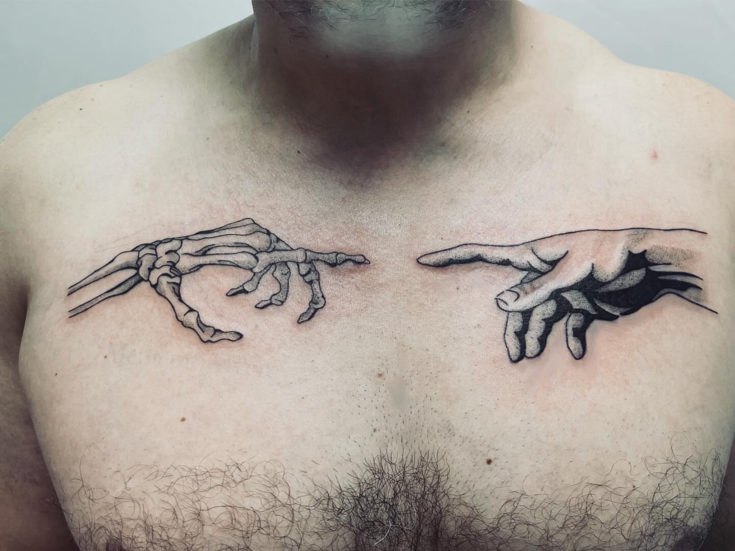 Skeleton hand reaching towards another hand black and grey tattoo on the chest by vivian