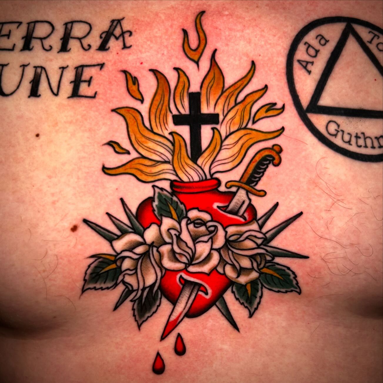 Burning heart with cross and dagger American traditional tattoo on the chest by Katie Dexter, Des Moines, Iowa