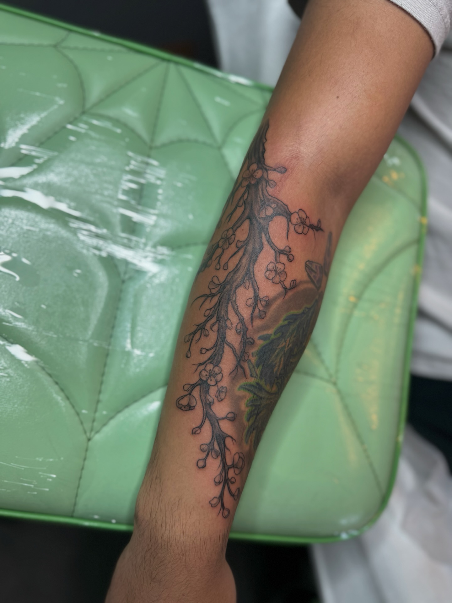 Root system with blossoms black and grey tattoo on the forearm by Lily Bejarno