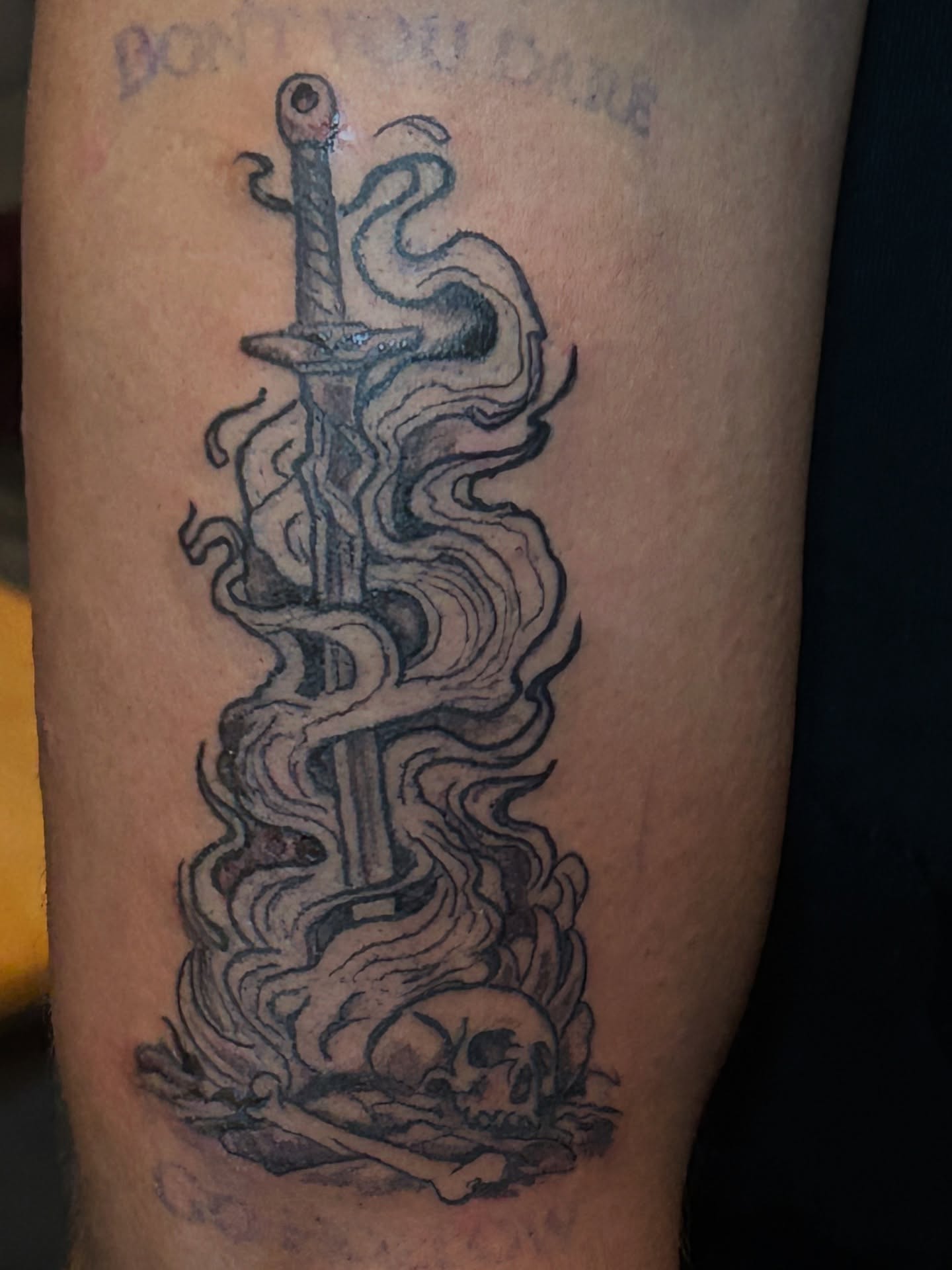 Sword and smoke black and grey tattoo on the forearm by Trae