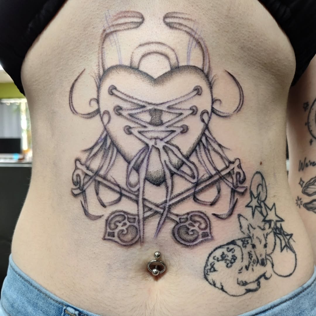 Heart with laces black and grey tattoo on the torso by Julie MacDonald