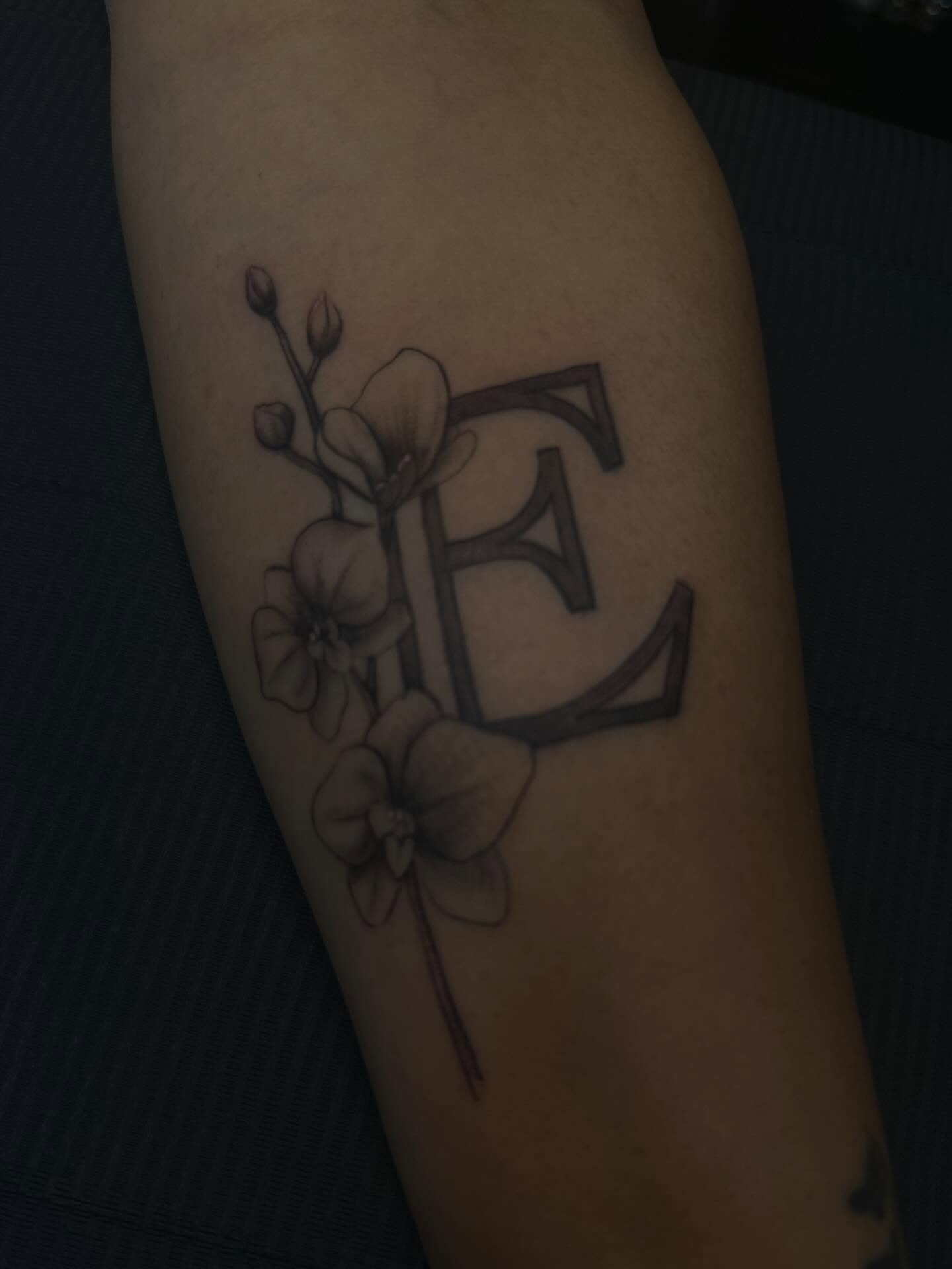 Flower and letter E black and grey tattoo on the forearm by Inked By E, Philadelphia, Pennsylvania
