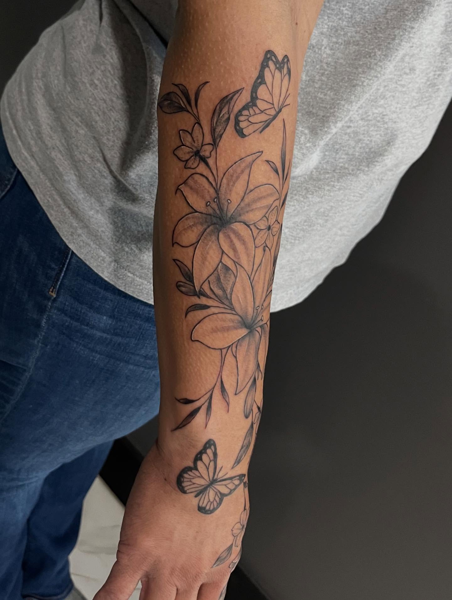 Flowers and butterflies black and grey tattoo on the forearm by Lexi Odam