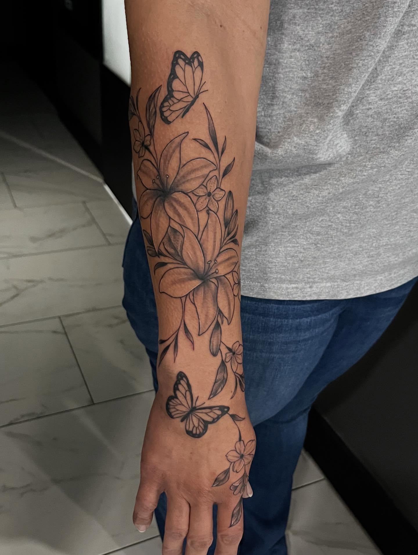 Lilies and butterflies black and grey tattoo on the forearm by Lexi Odam