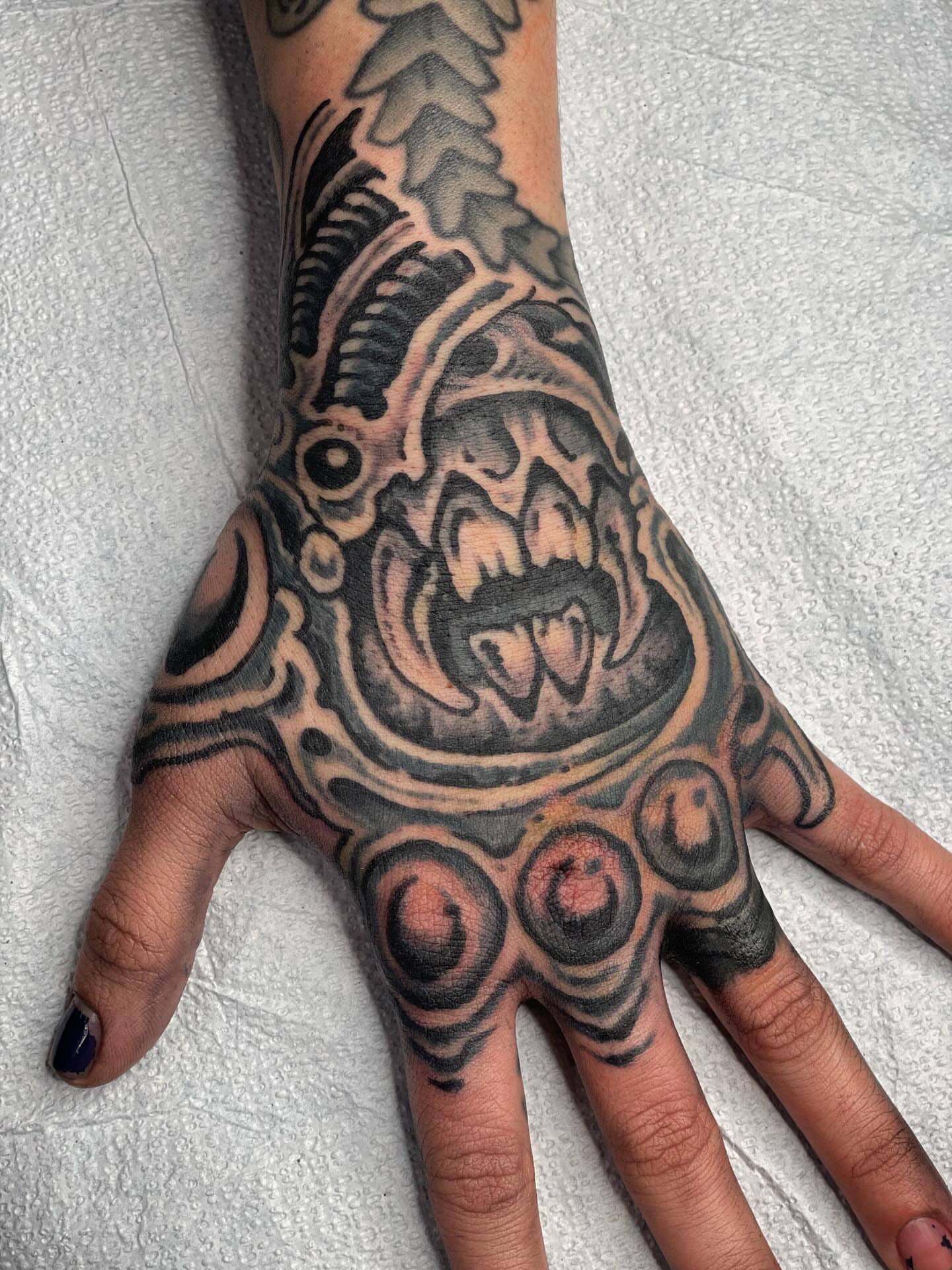 Demon face black and grey tattoo on the hand by Zac Blevins