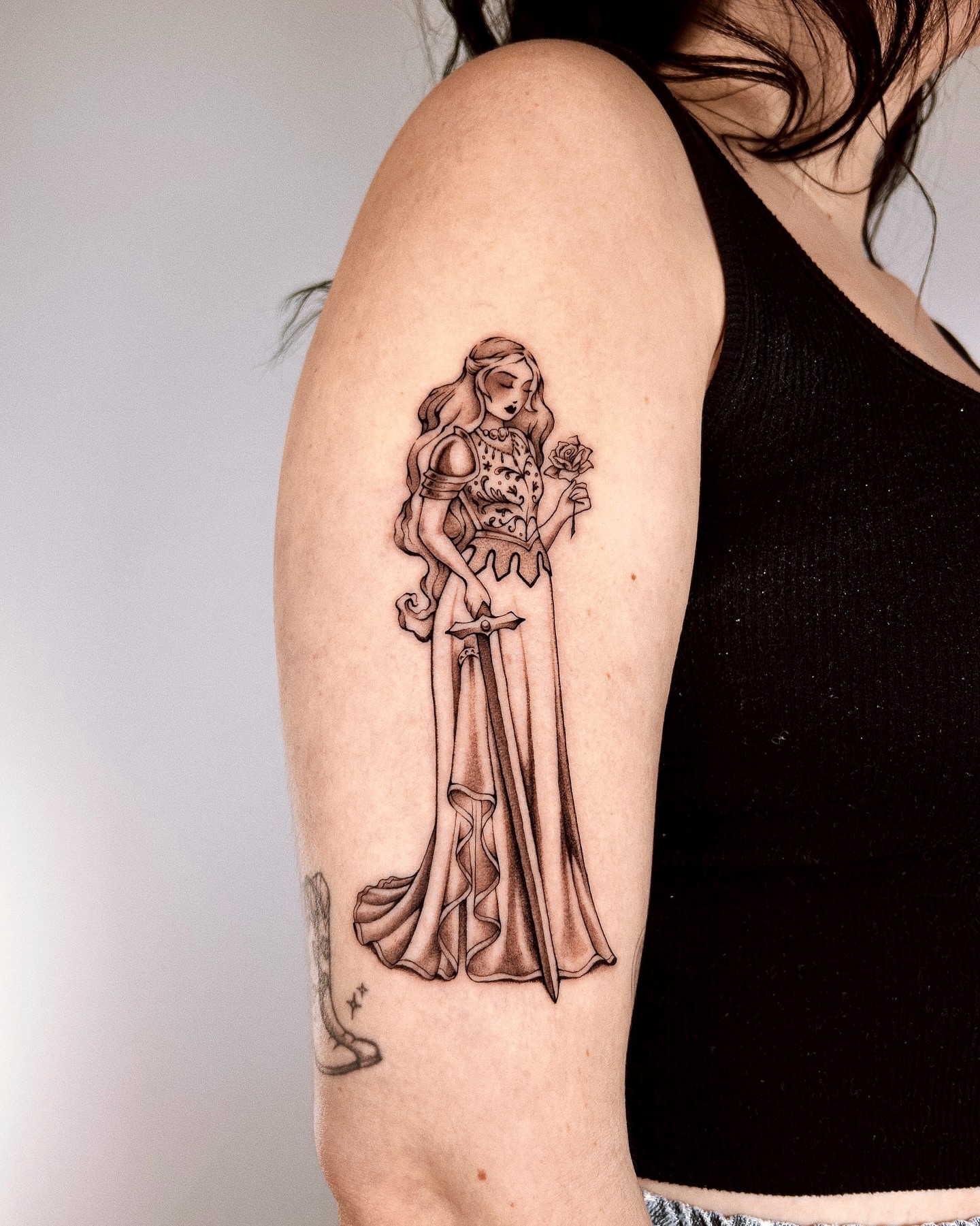 Woman with rose black and grey tattoo on the upper arm by Montana Chambers