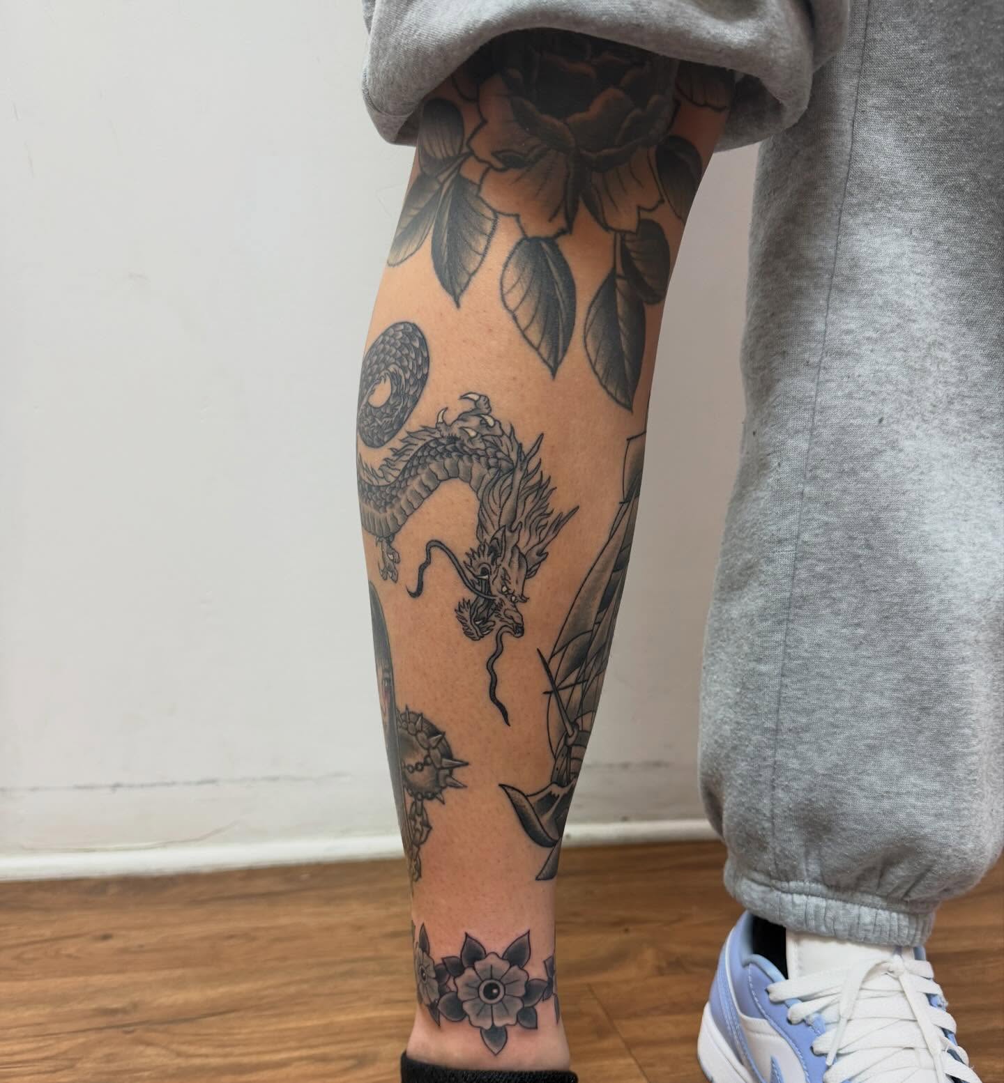 Dragon and flowers black and grey tattoo on the calf by McKenna Chalifoux
