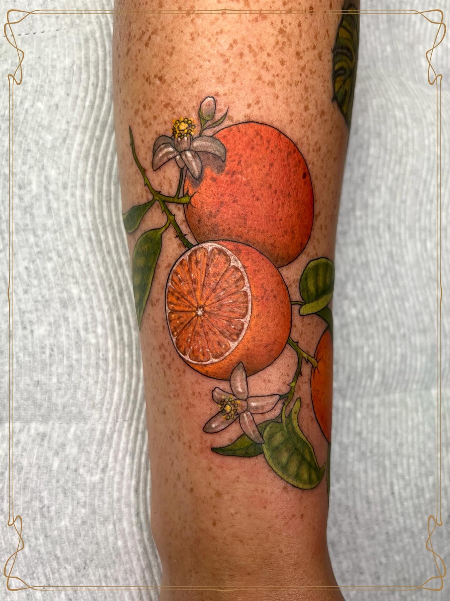 Orange and flowers realism tattoo on the forearm by Severin Black