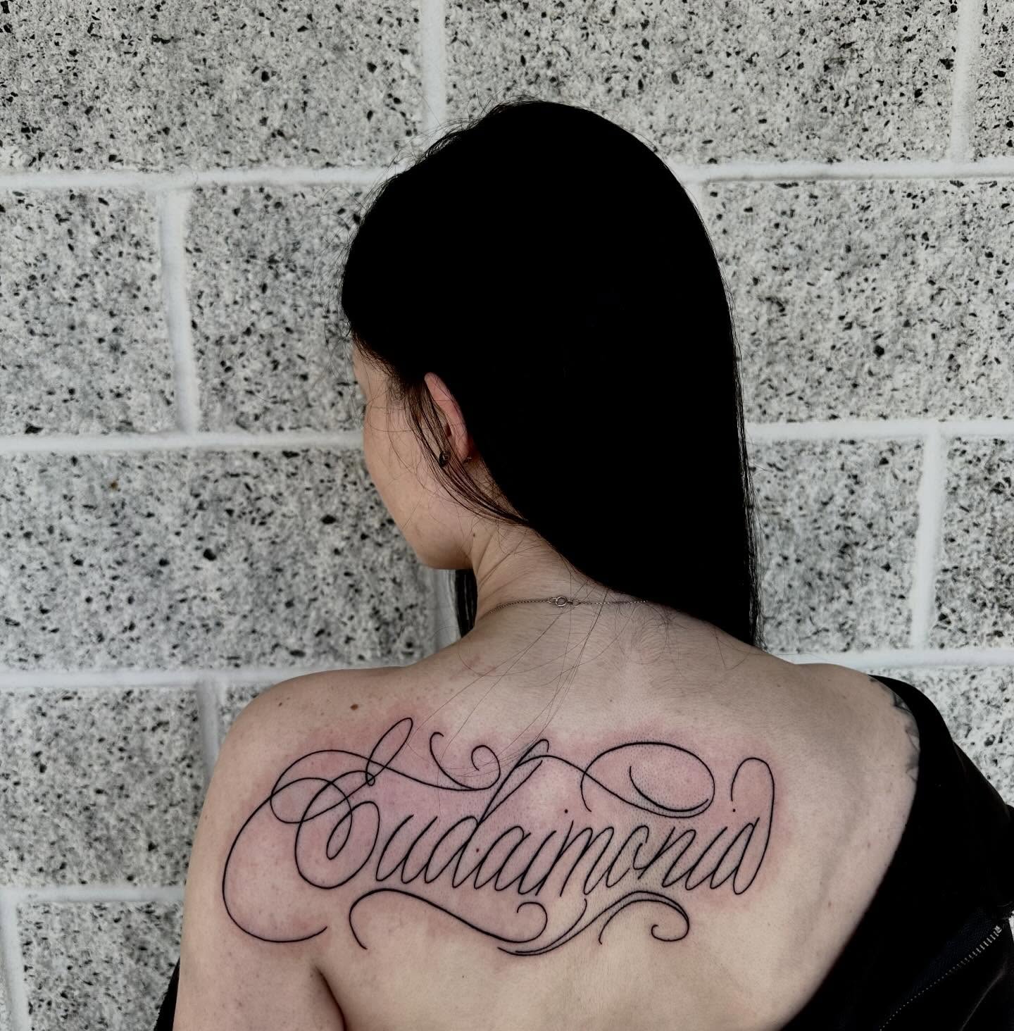 Eudaimonia lettering script tattoo on the back by emma christine