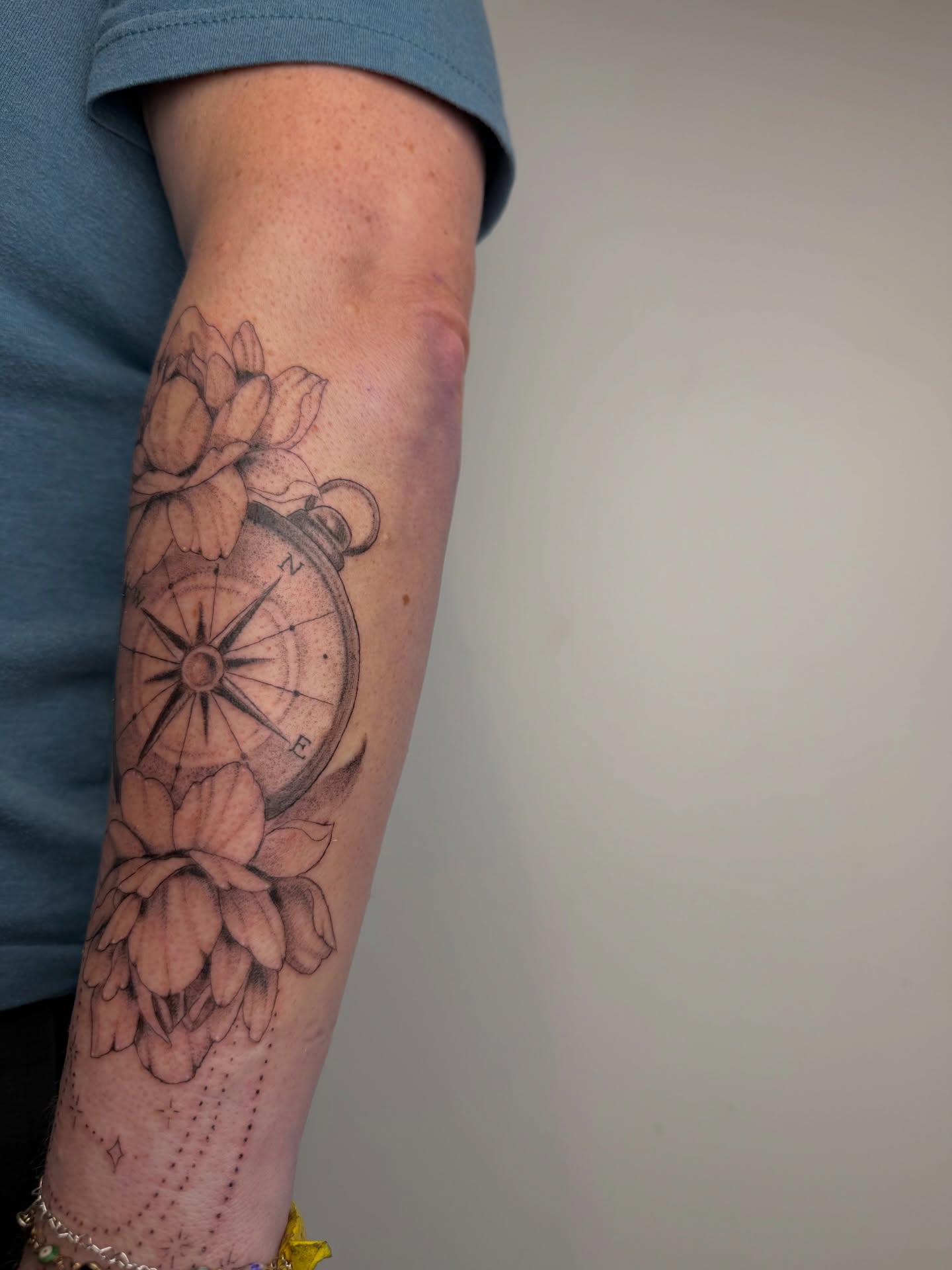 Compass and flowers black and grey tattoo on the forearm by Mackenzie