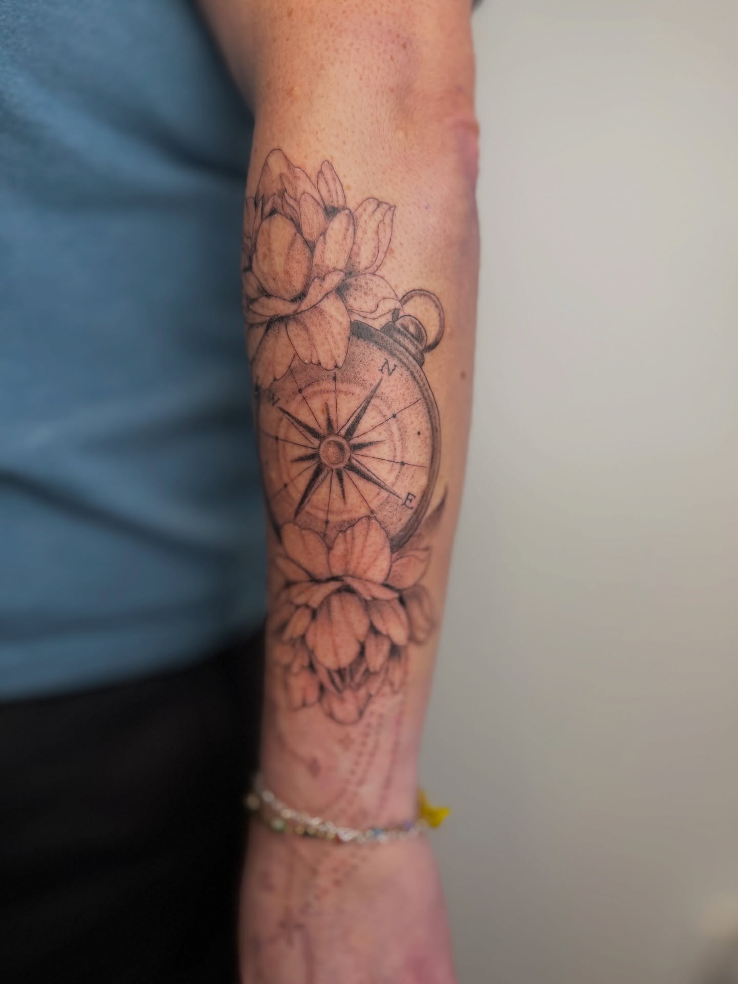 Compass and flowers black and grey tattoo on the forearm by Mackenzie