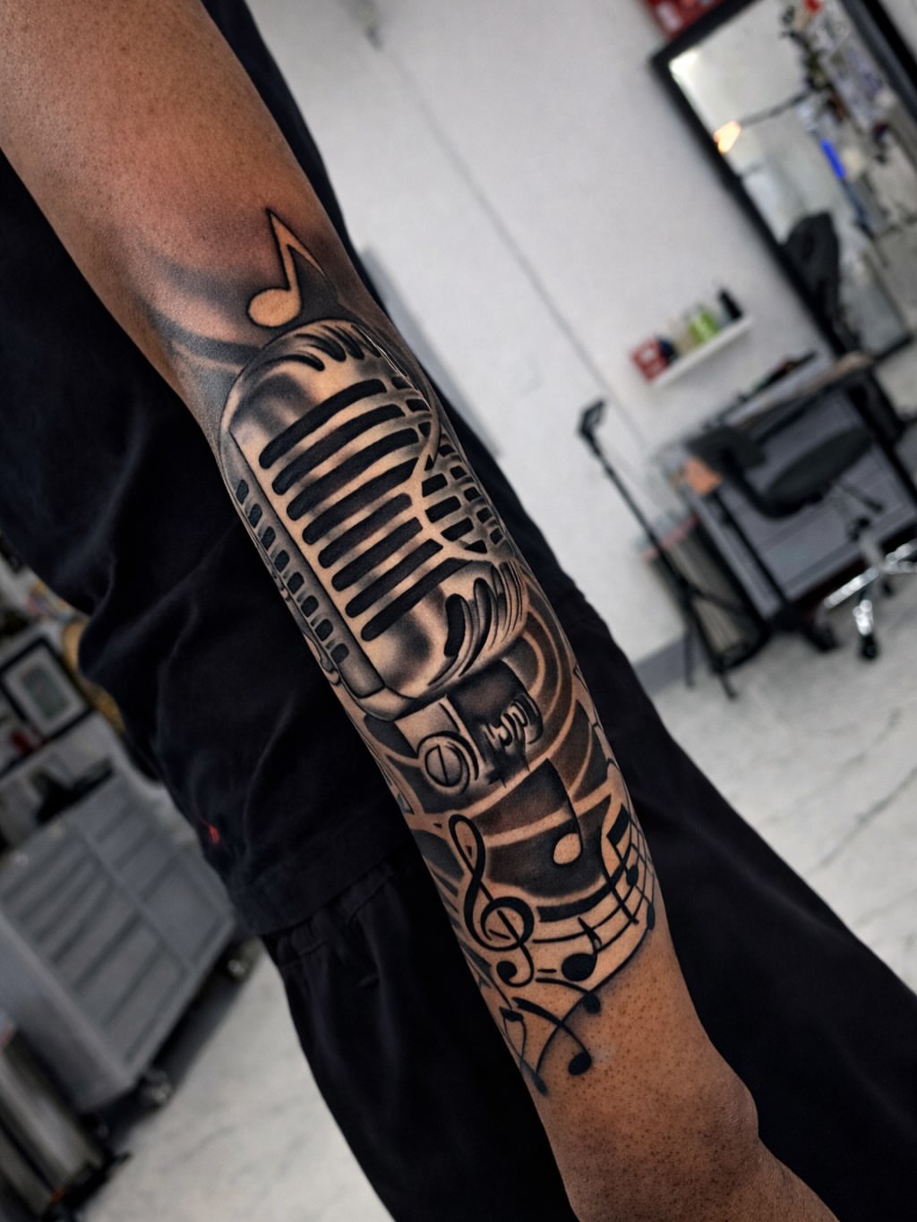 Microphone and musical notes black and grey tattoo on the forearm by Jaylen - Atlanta Tattoo Artist