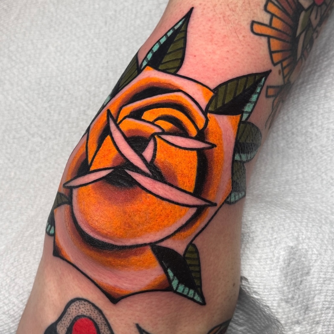 Orange rose American traditional tattoo on the forearm by Jess Baker