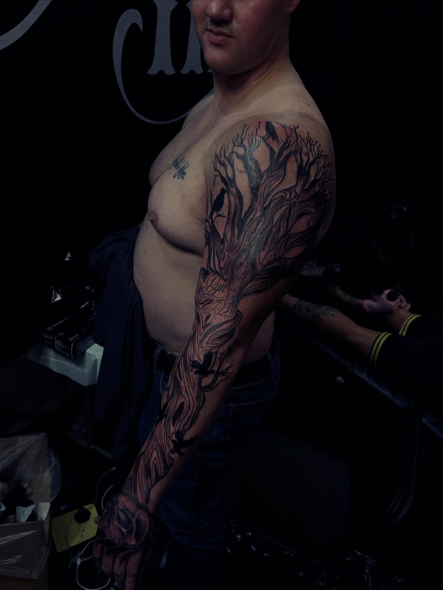 Tree with birds black and grey tattoo on the upper arm by Rell Washington, Marlow Heights, Maryland