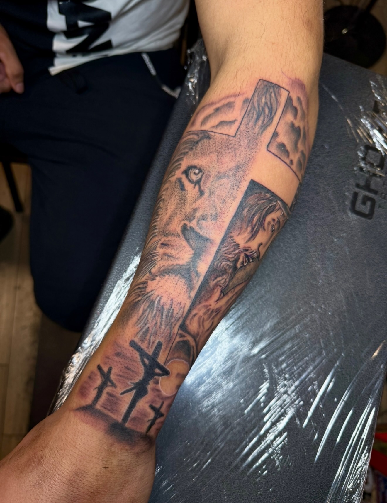 Lion and cross realism tattoo on the forearm by Zac Clark