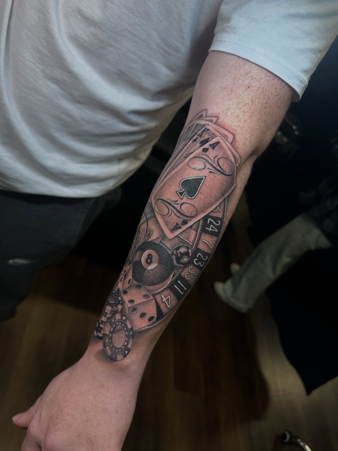 Playing cards and pool ball black and grey tattoo on the forearm by Priscilla Michels