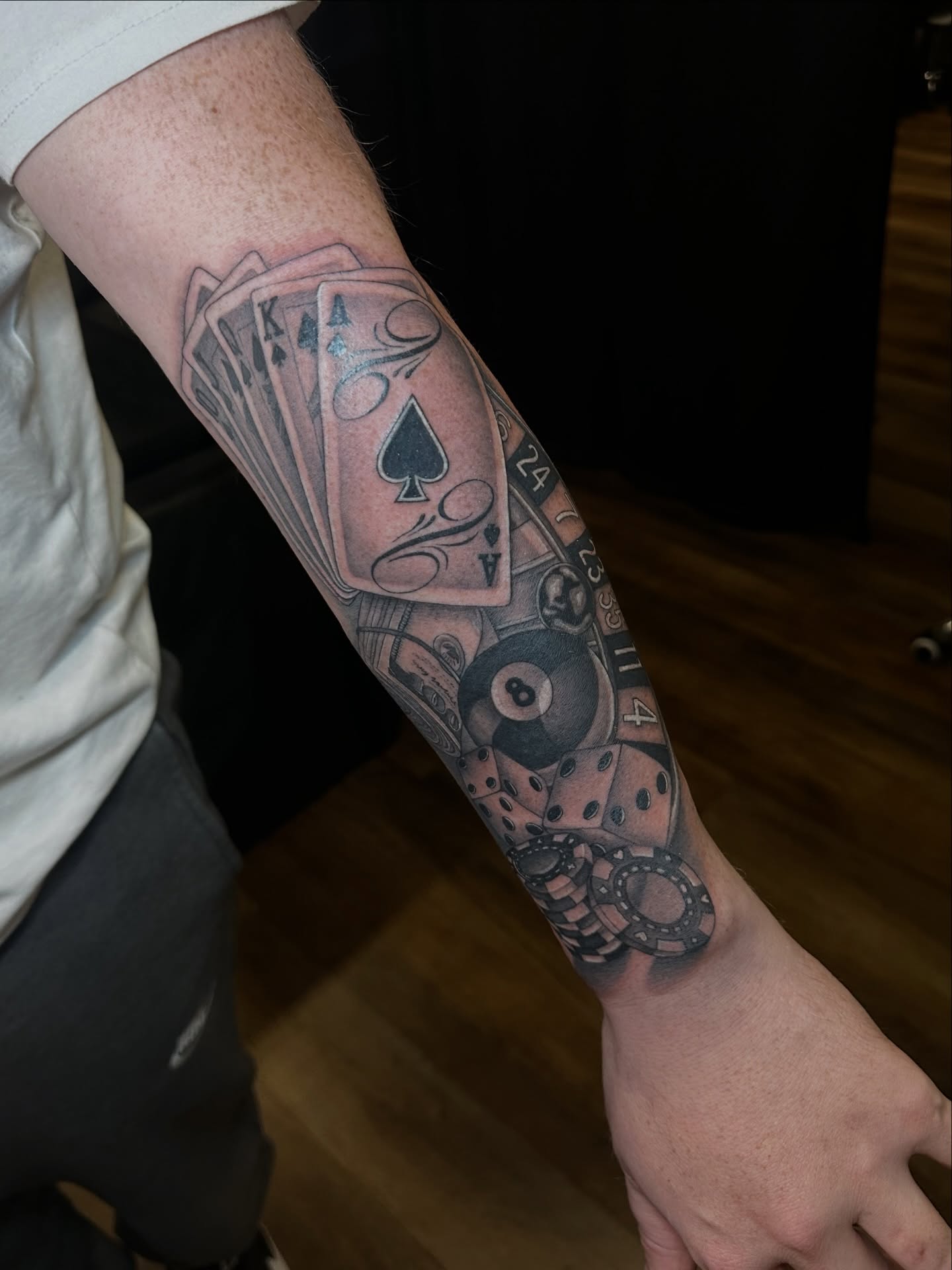 Playing cards and dice black and grey tattoo on the forearm by Priscilla Michels