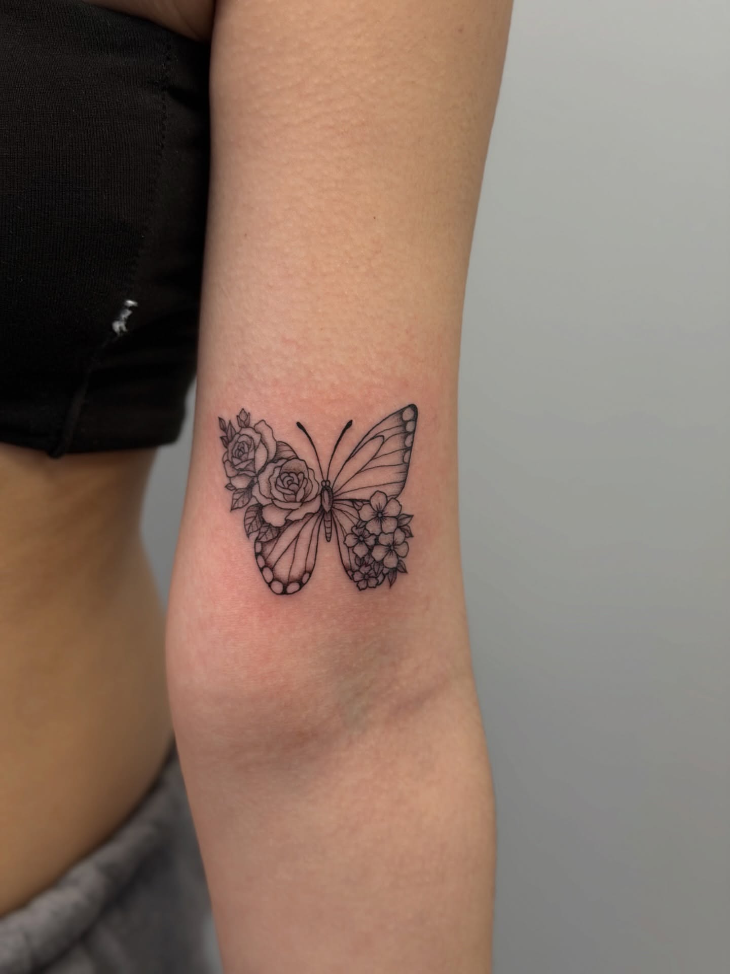Butterfly and flowers black and grey tattoo on the forearm by Mandy Kaur