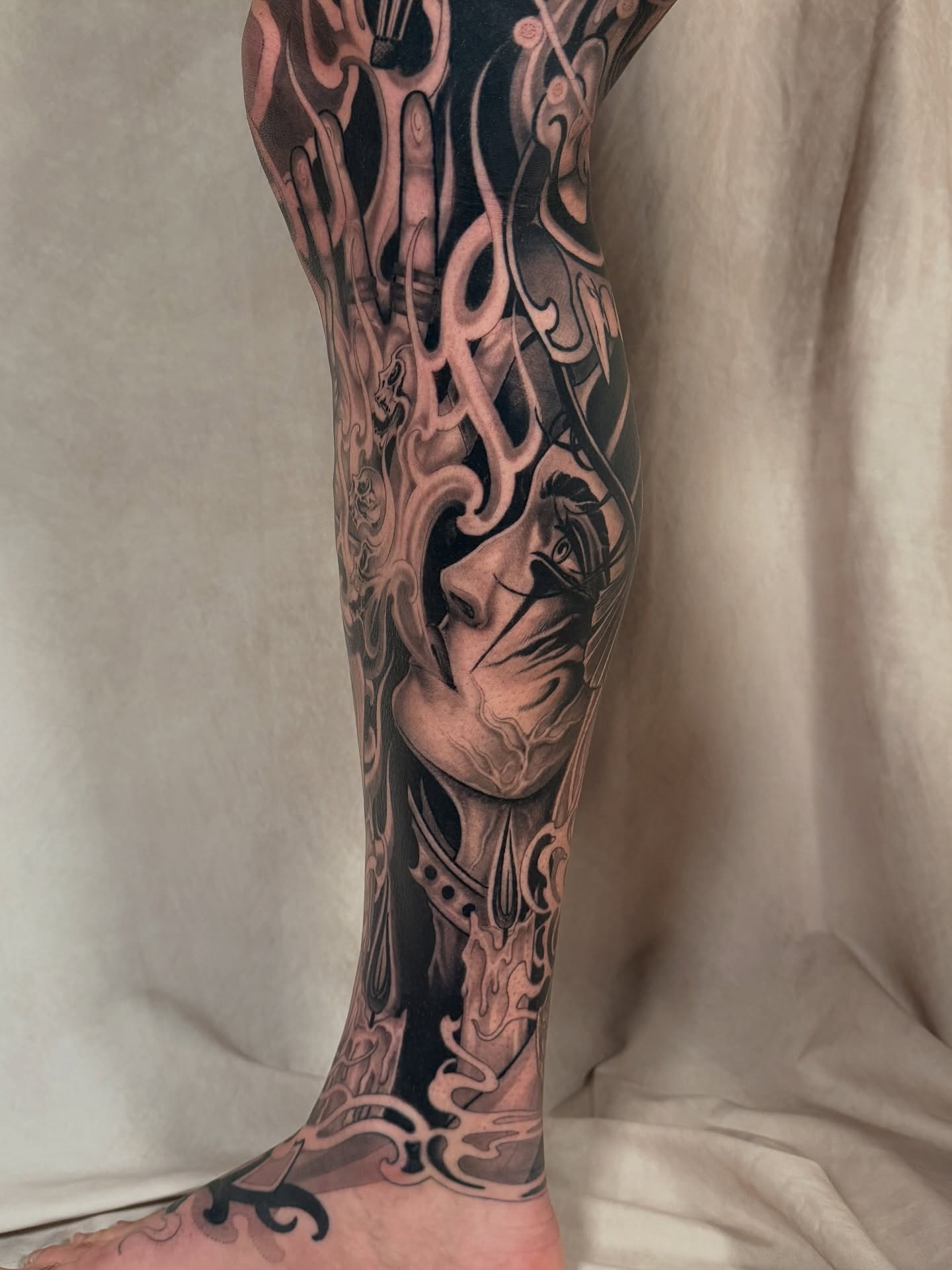 Abstract face dark realism tattoo on the calf by <