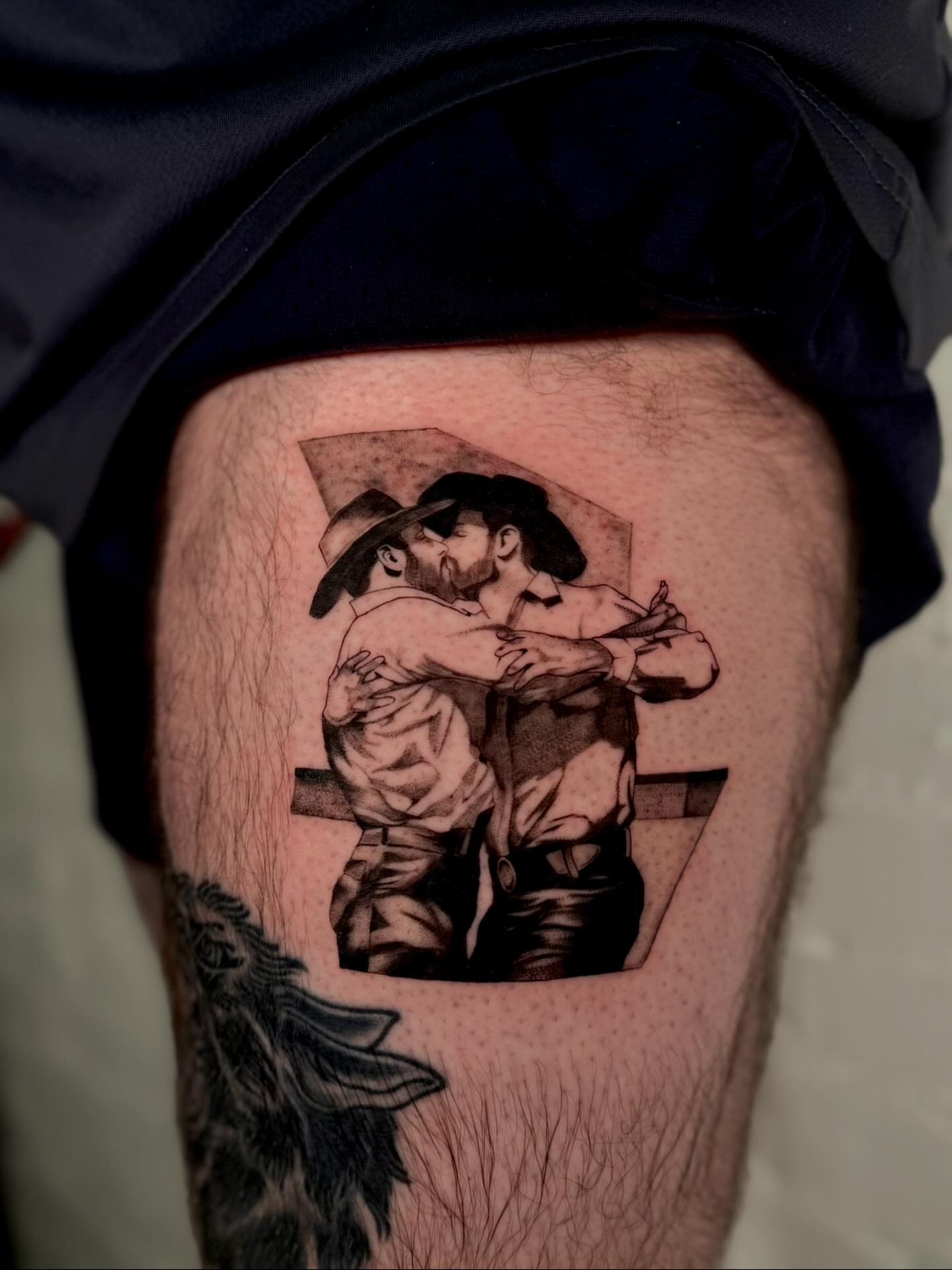 Kissing couple black and grey tattoo on the thigh by Hayley Jude
