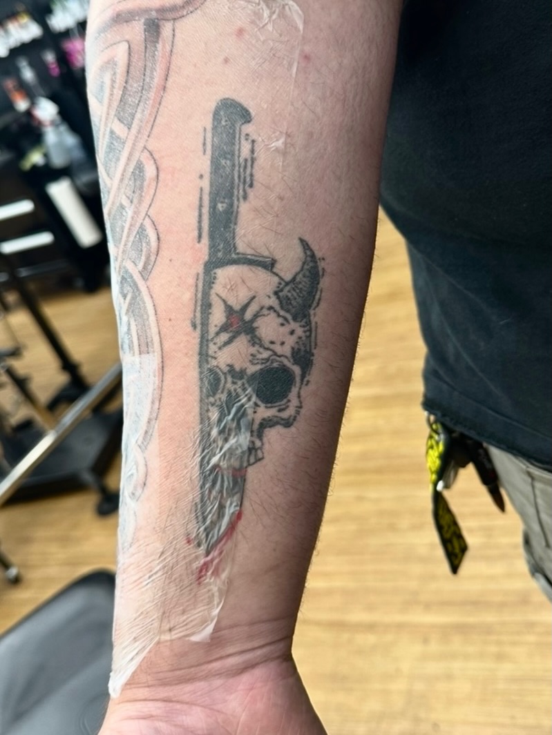 Skull and gun black and grey tattoo on the forearm by Tyler Reep