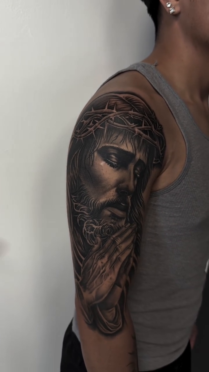 Jesus Christ praying Chicano tattoo on the upper arm by Hugo Ruiz-Esparza