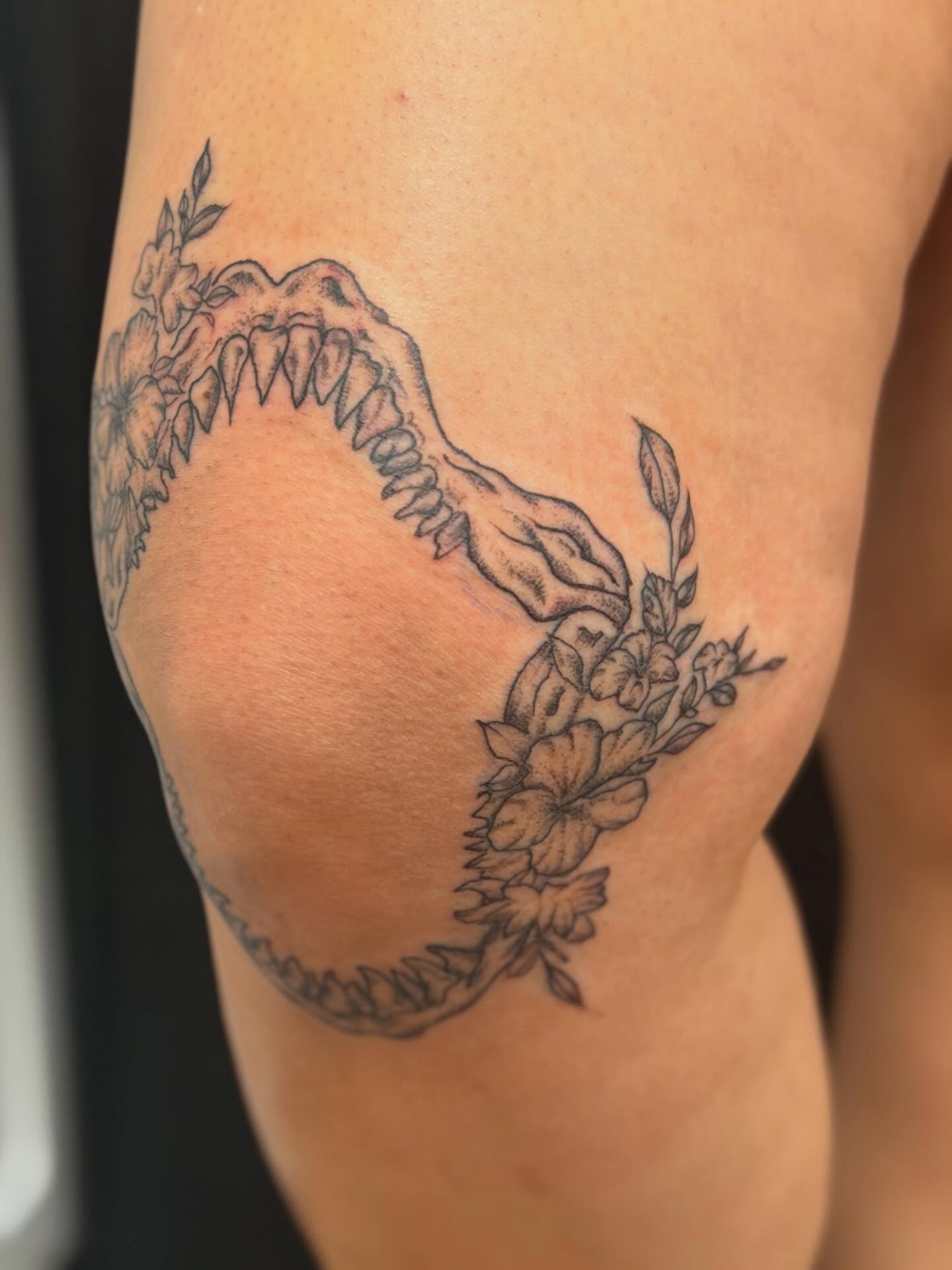Dinosaur skull with flowers black and grey tattoo on the thigh by cortez