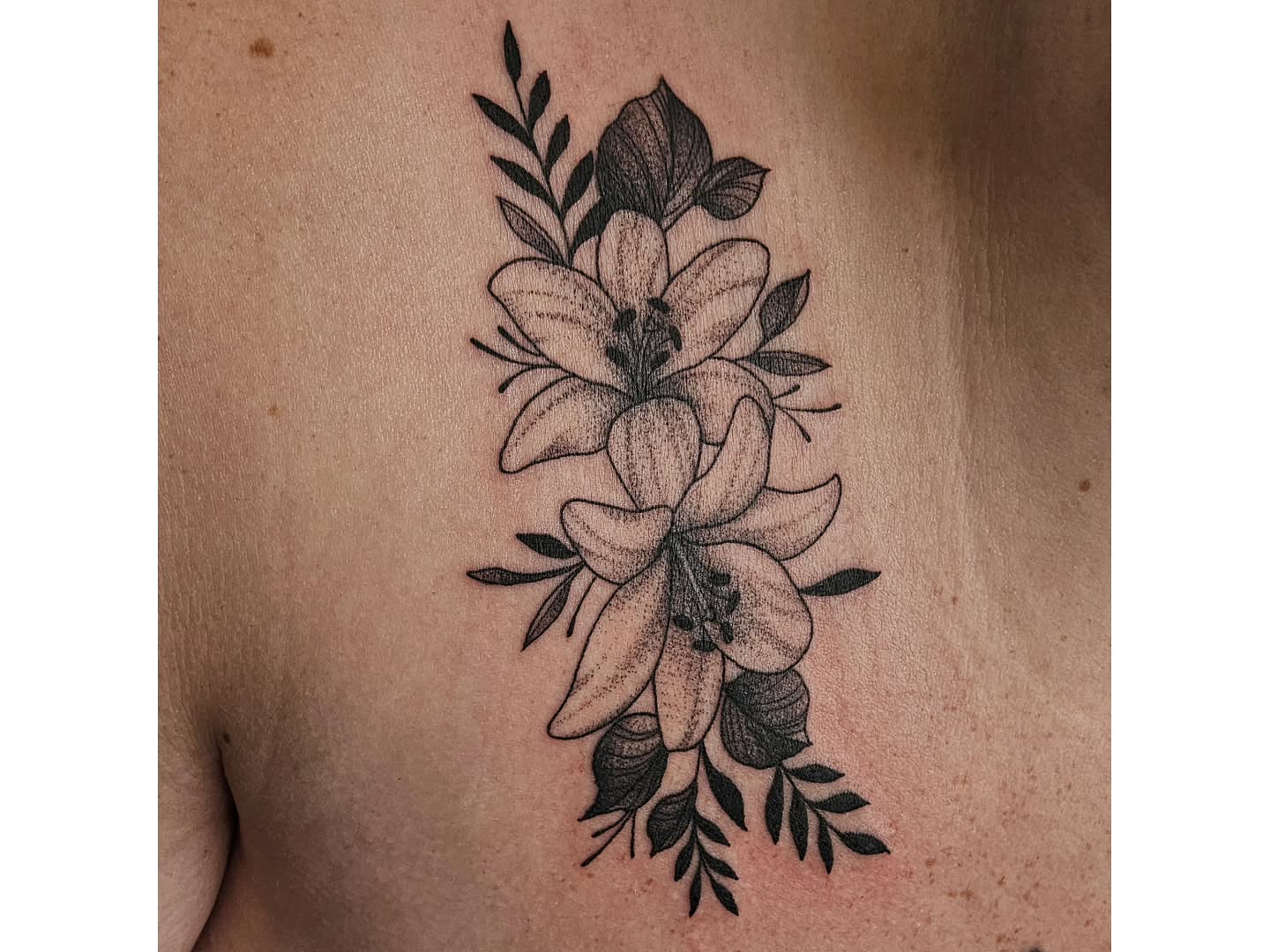 Lilies and leaves black and grey tattoo on the back by Kylie Lund