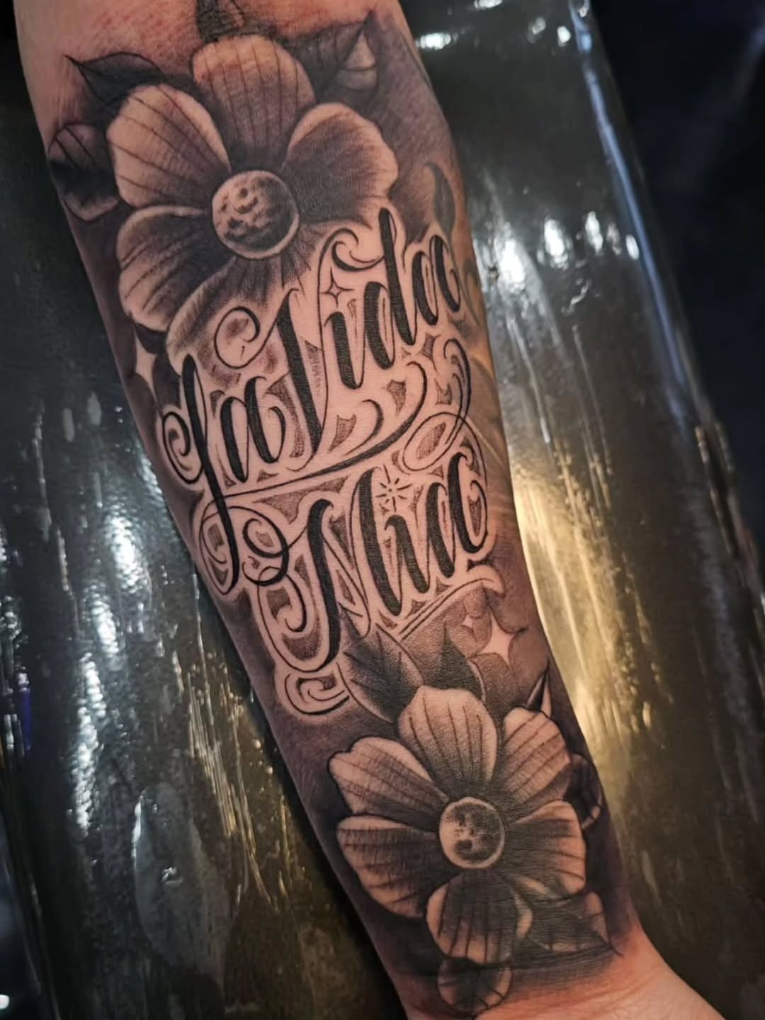 Flower and script black and grey tattoo on the forearm by Richie Garcia, Hesperia, California