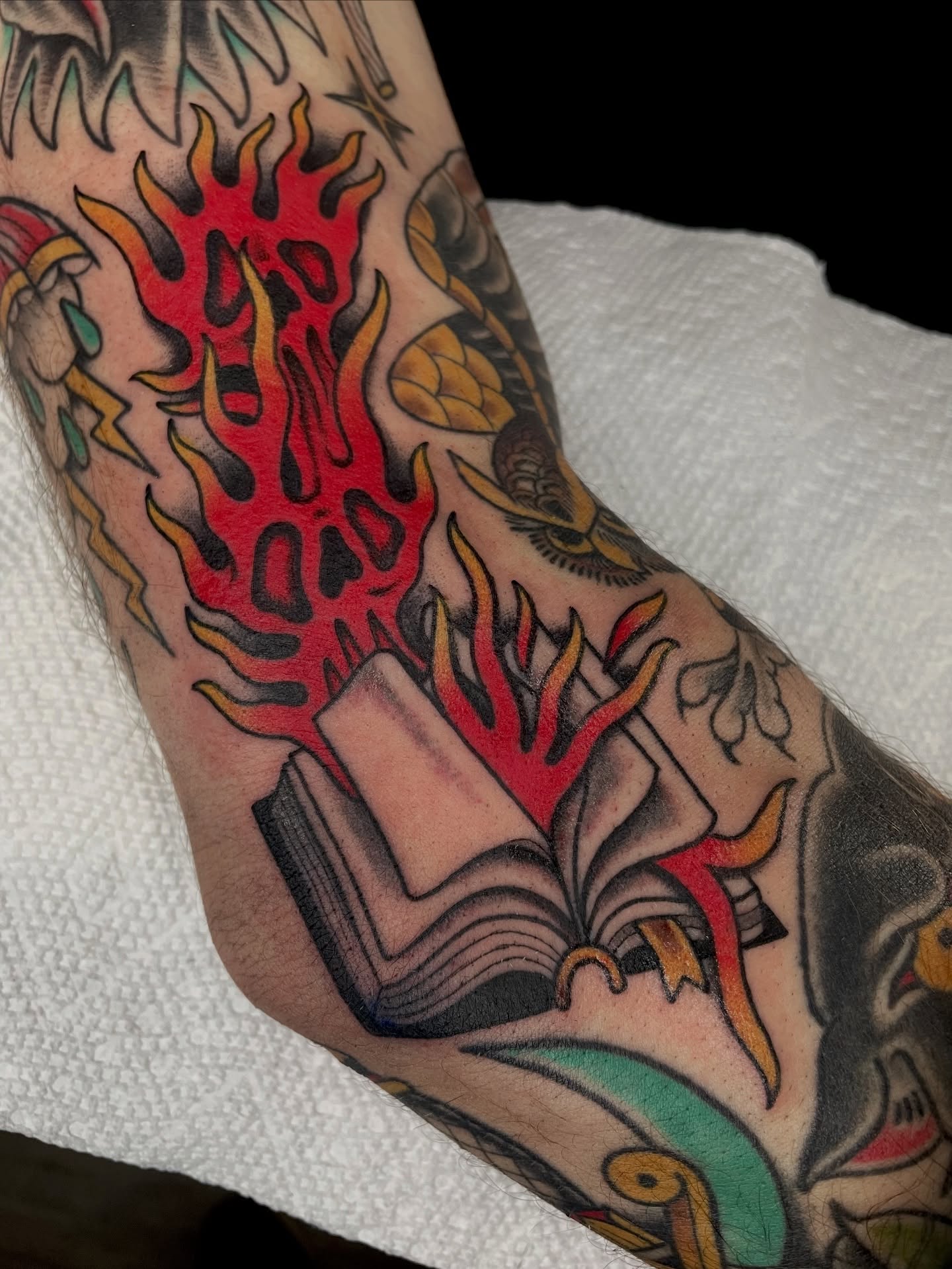 Flaming book American traditional tattoo on the forearm by Josh Johns