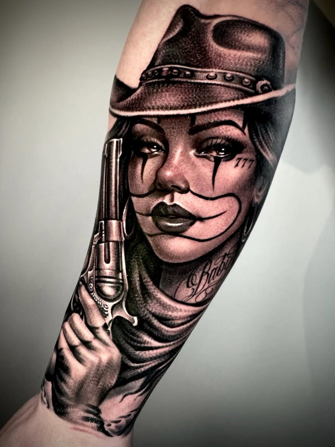 Woman with gun and hat Chicano tattoo on the forearm by David Torres