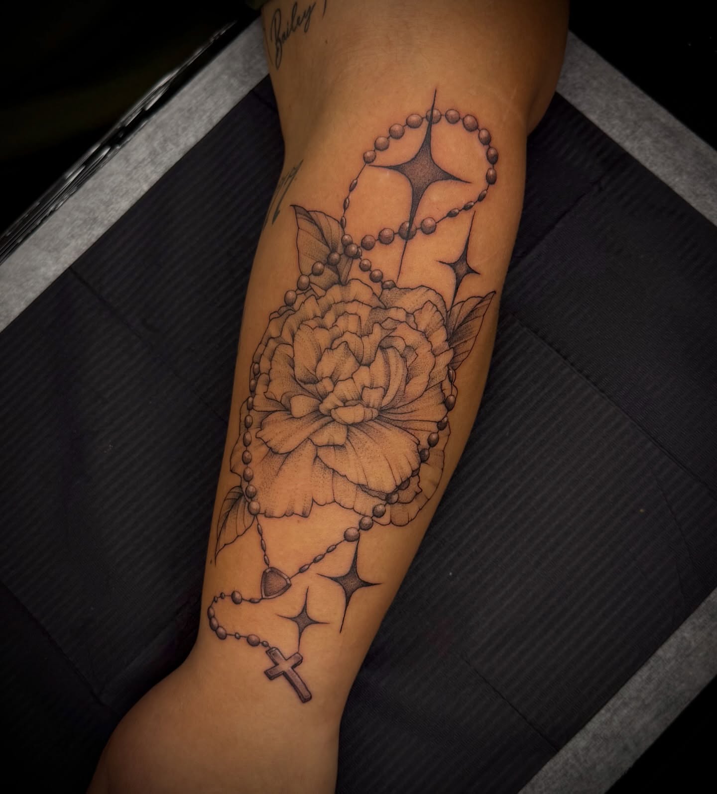 Rosary and flower black and grey tattoo on the forearm by Marcus