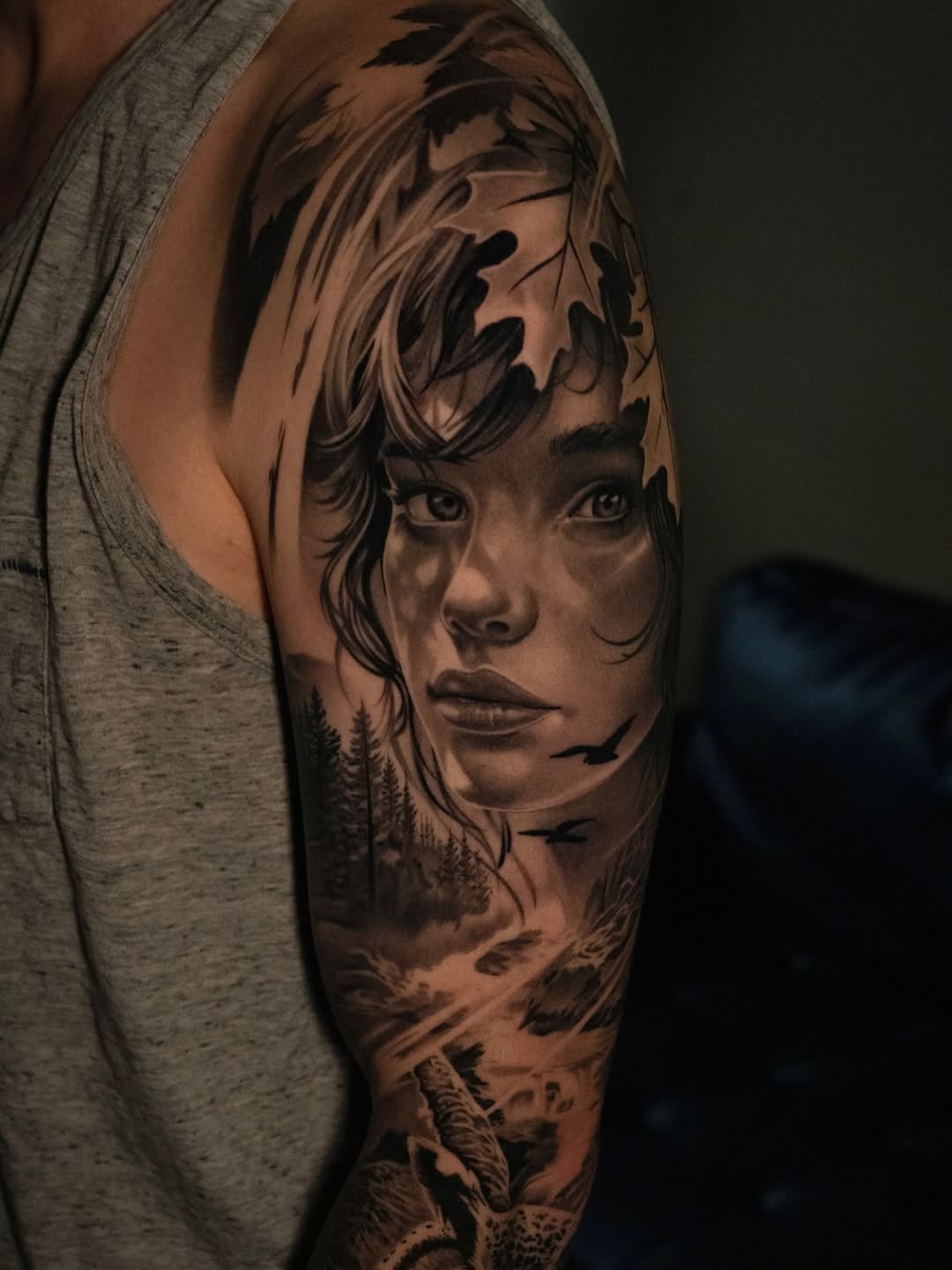 Woman's portrait with landscape realism tattoo on the upper arm by @kotytattoos