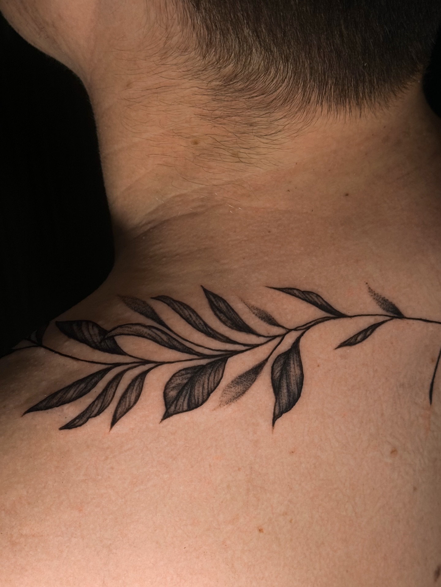 Branch with leaves black and grey tattoo on the neck by Kam Mills