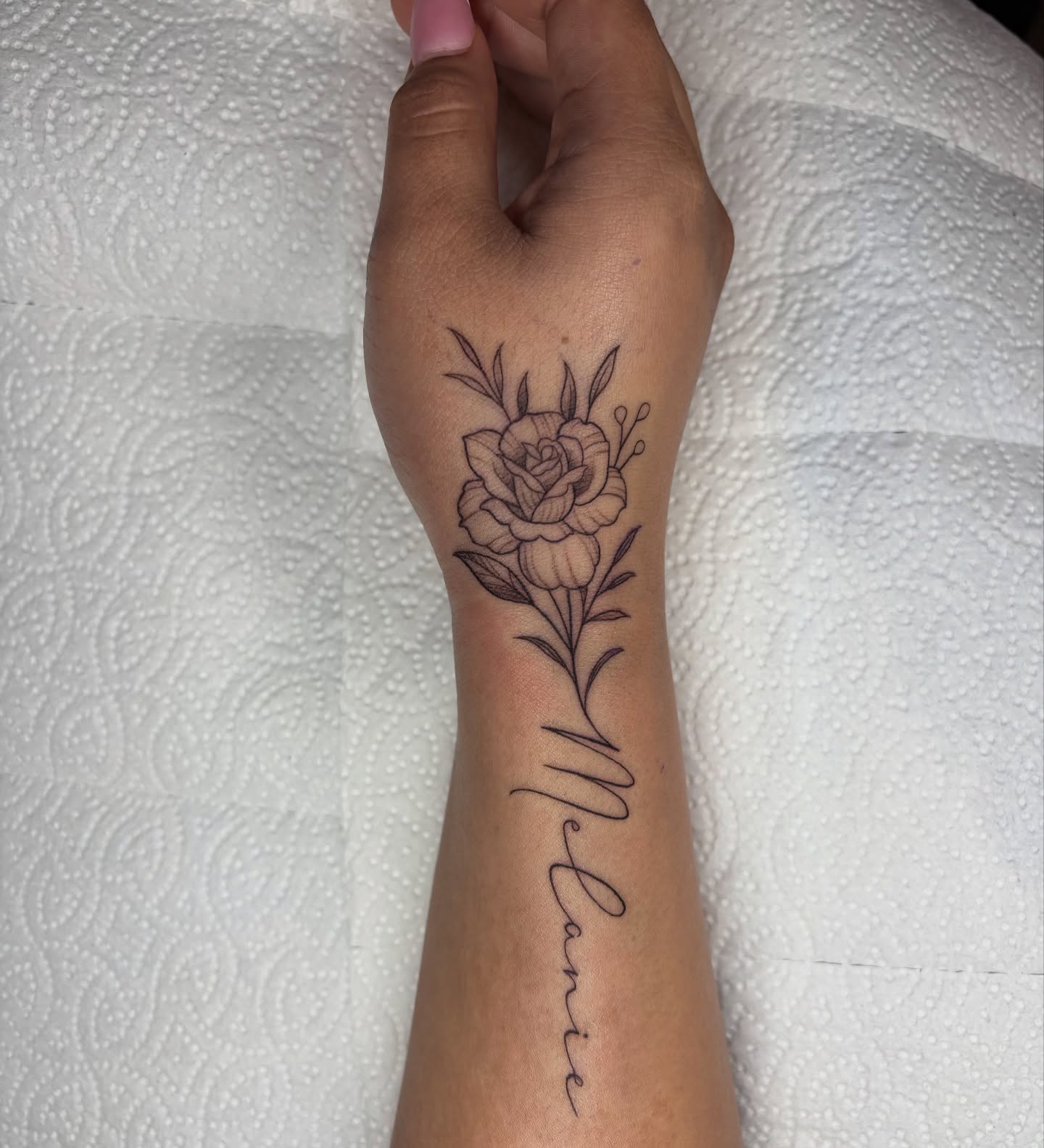 Flower and name black and grey tattoo on the forearm by Fineline tattoos by Kinsey