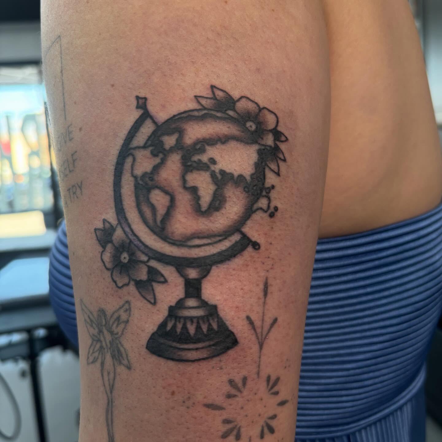 Globe with floral crown black and grey tattoo on the forearm by Trevor