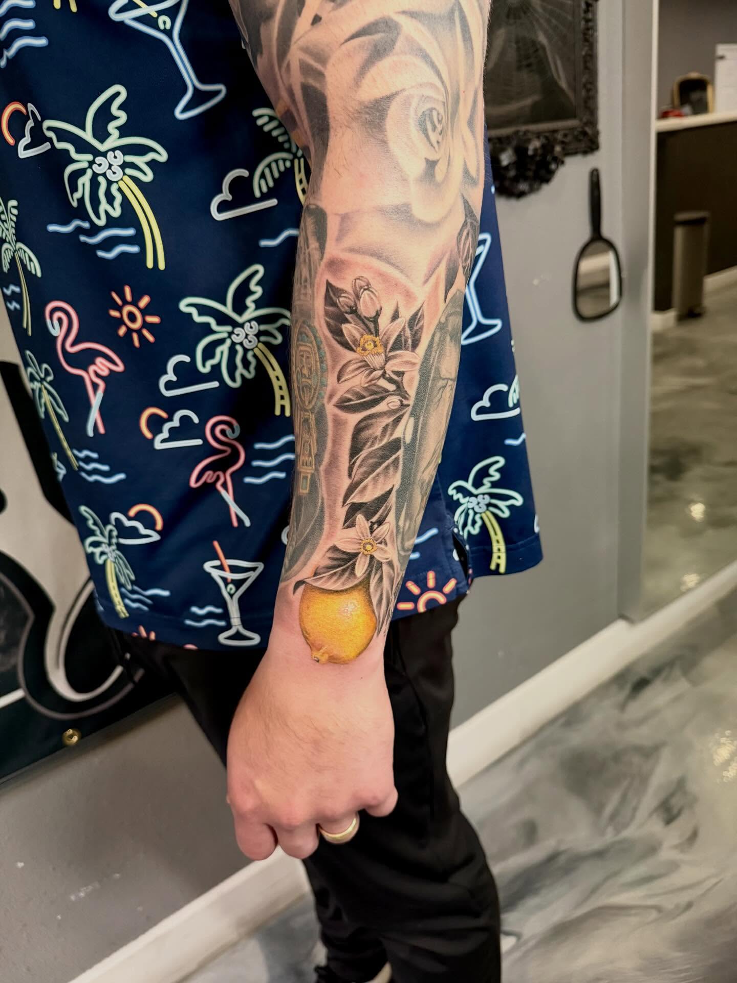 Lemon and flowers realism tattoo on the forearm by Cody Pappas