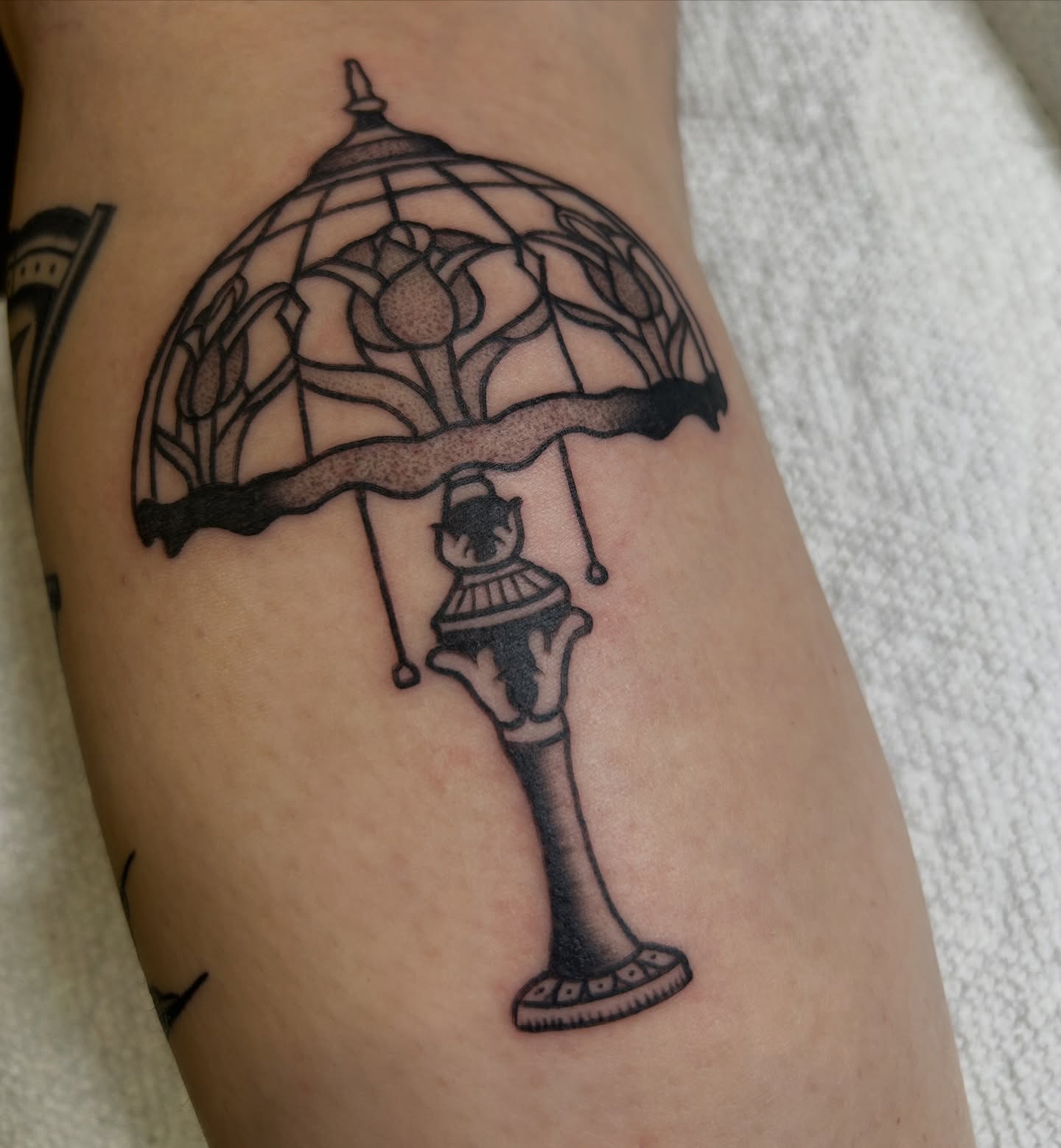 Lamp with floral umbrella black and grey tattoo on the forearm by Dylan James
